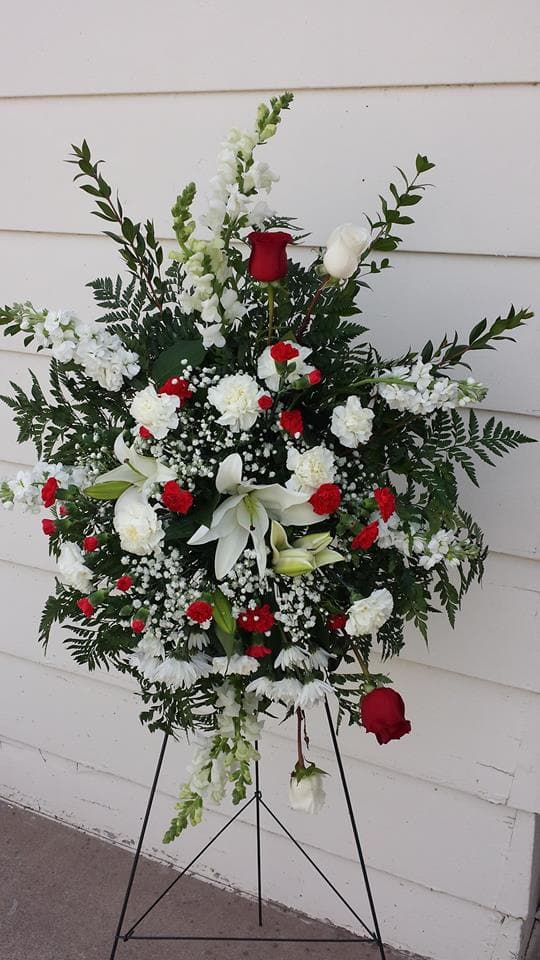Standing funeral spray with red and white flowers on a black easel