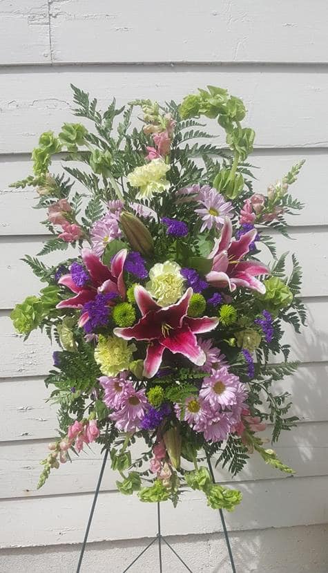 Standing floral spray with pink lilies and purple daisies on an easel