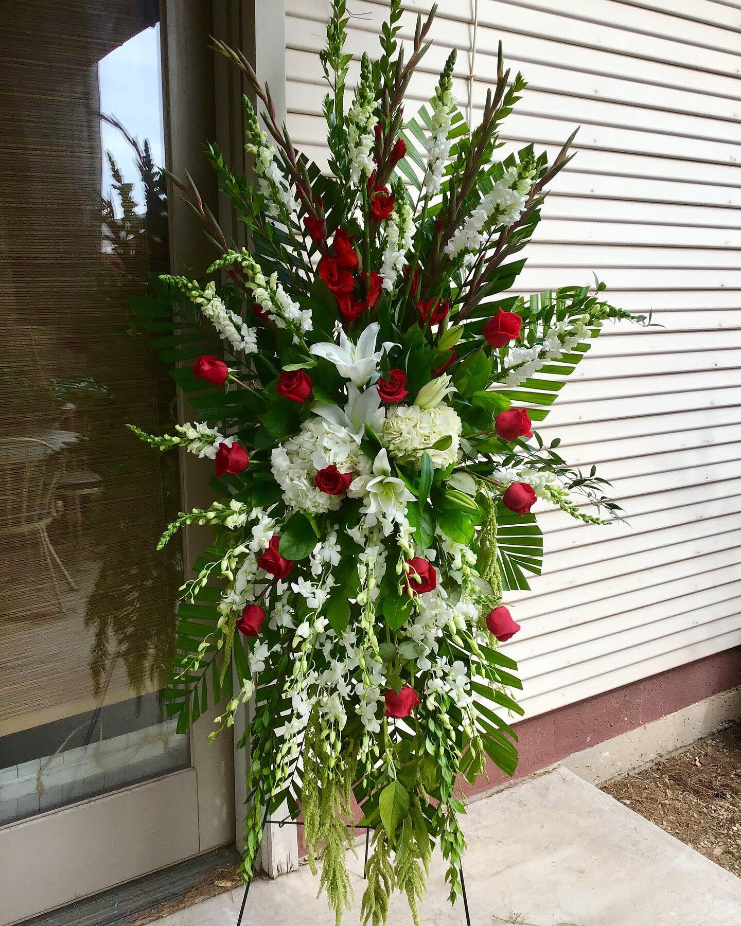 Standing floral spray with red roses and white lilies on a metal easel