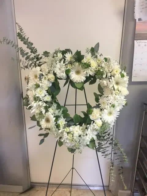 White floral wreath on a black stand with greenery accents