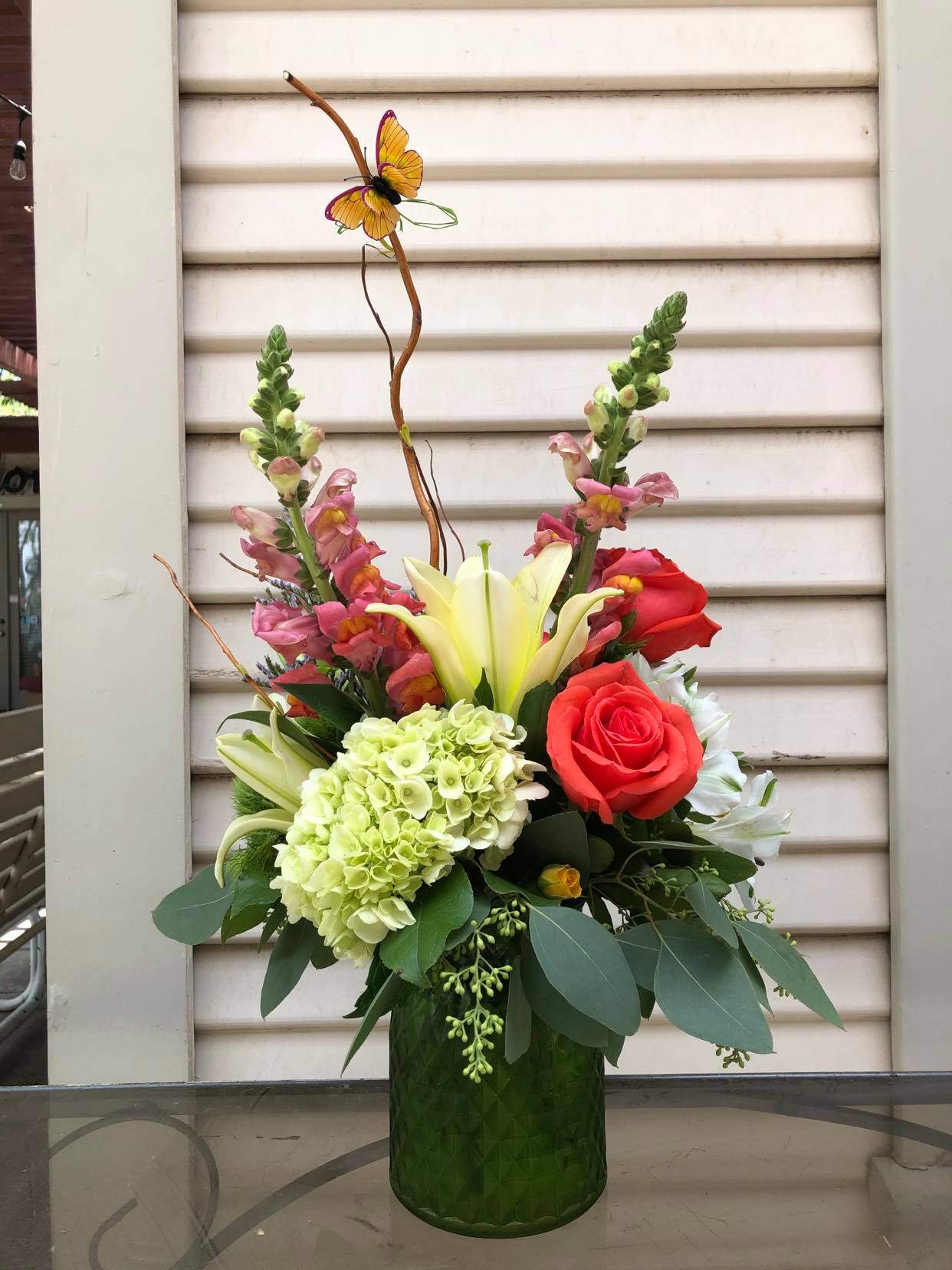 Mixed floral arrangement in a green vase with roses, lilies, and hydrangea