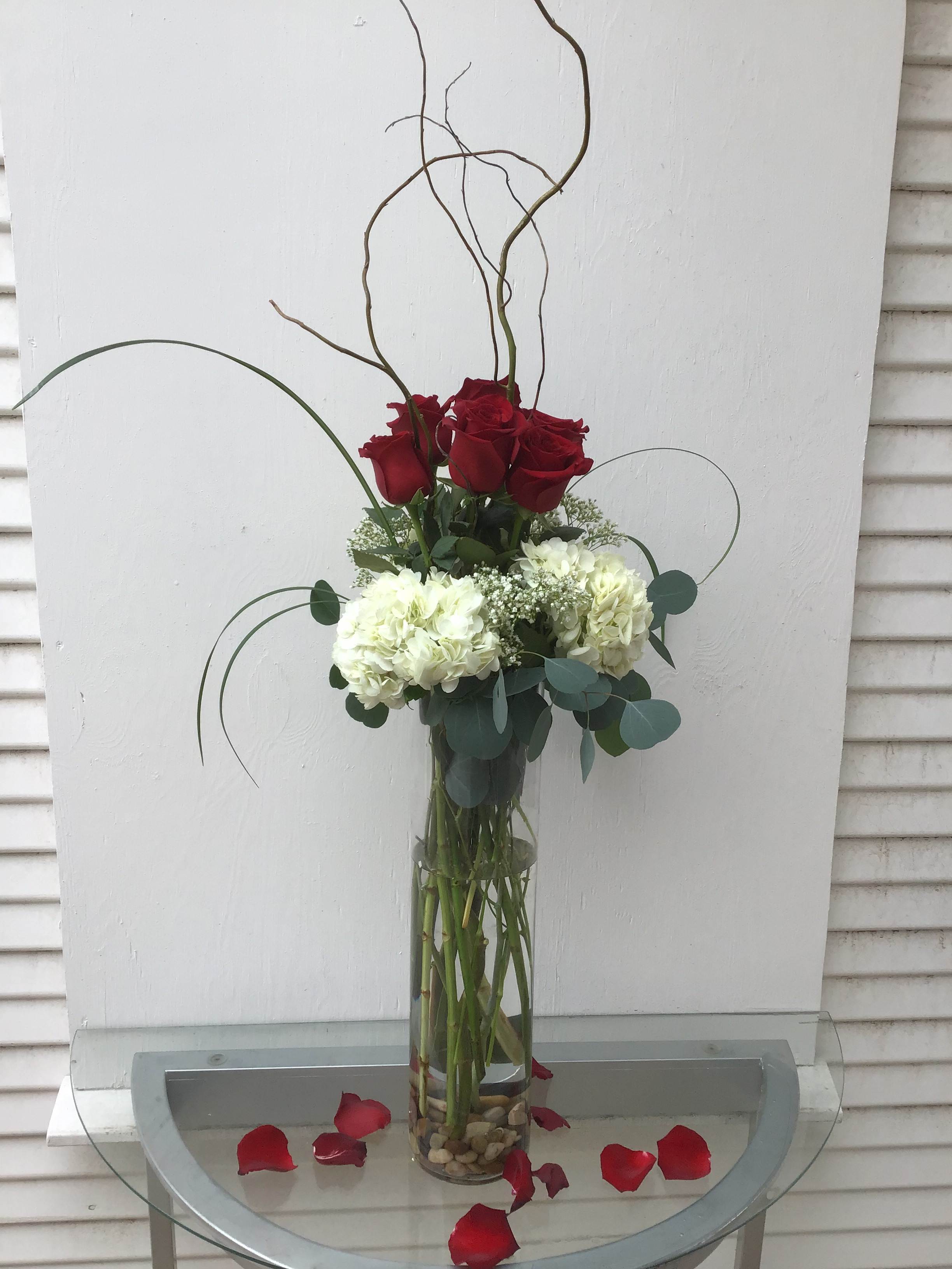 Tall vase arrangement of red roses and white hydrangeas with curly branches