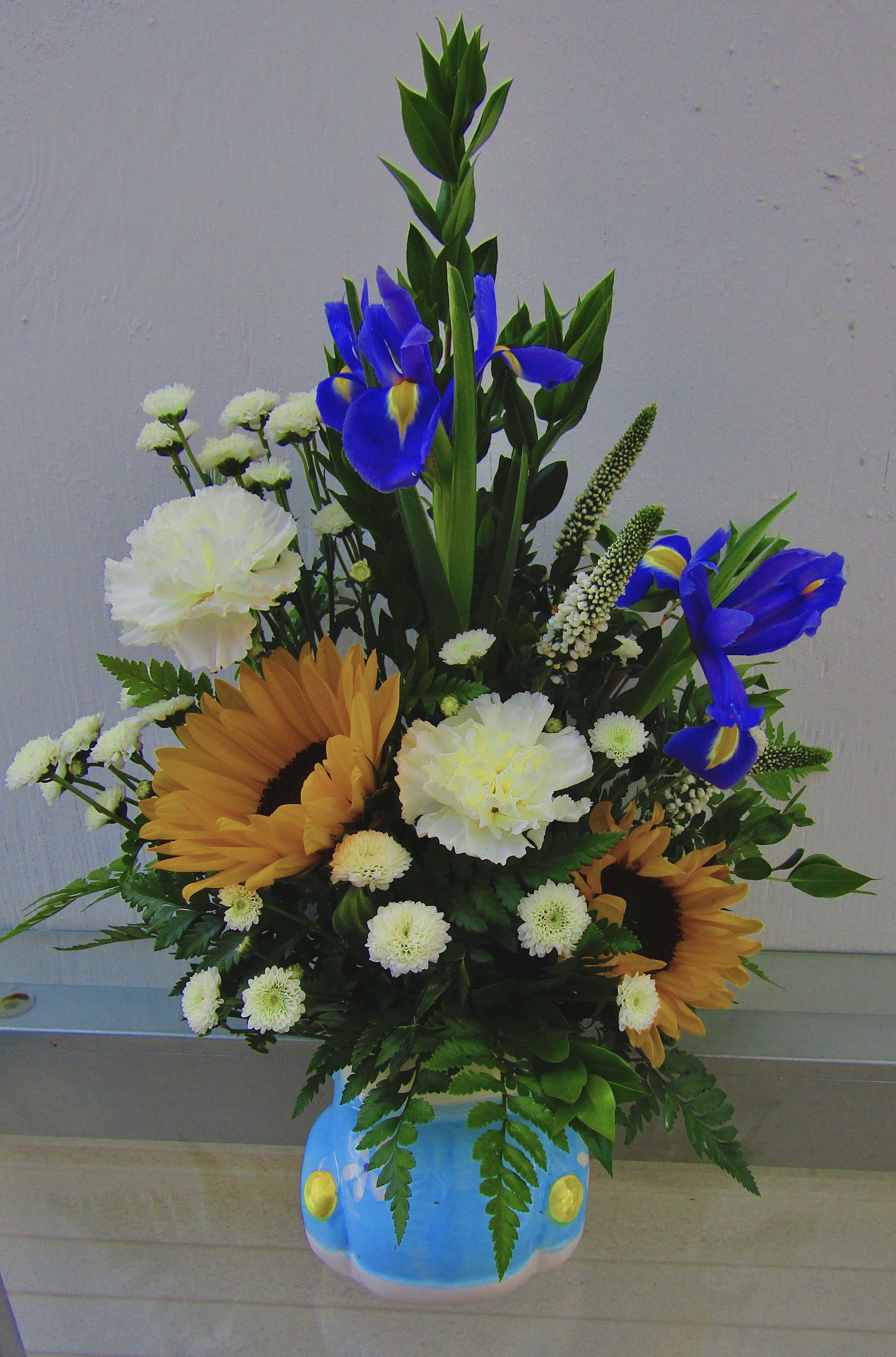 Bouquet with blue irises, sunflowers, and white carnations in a painted vase