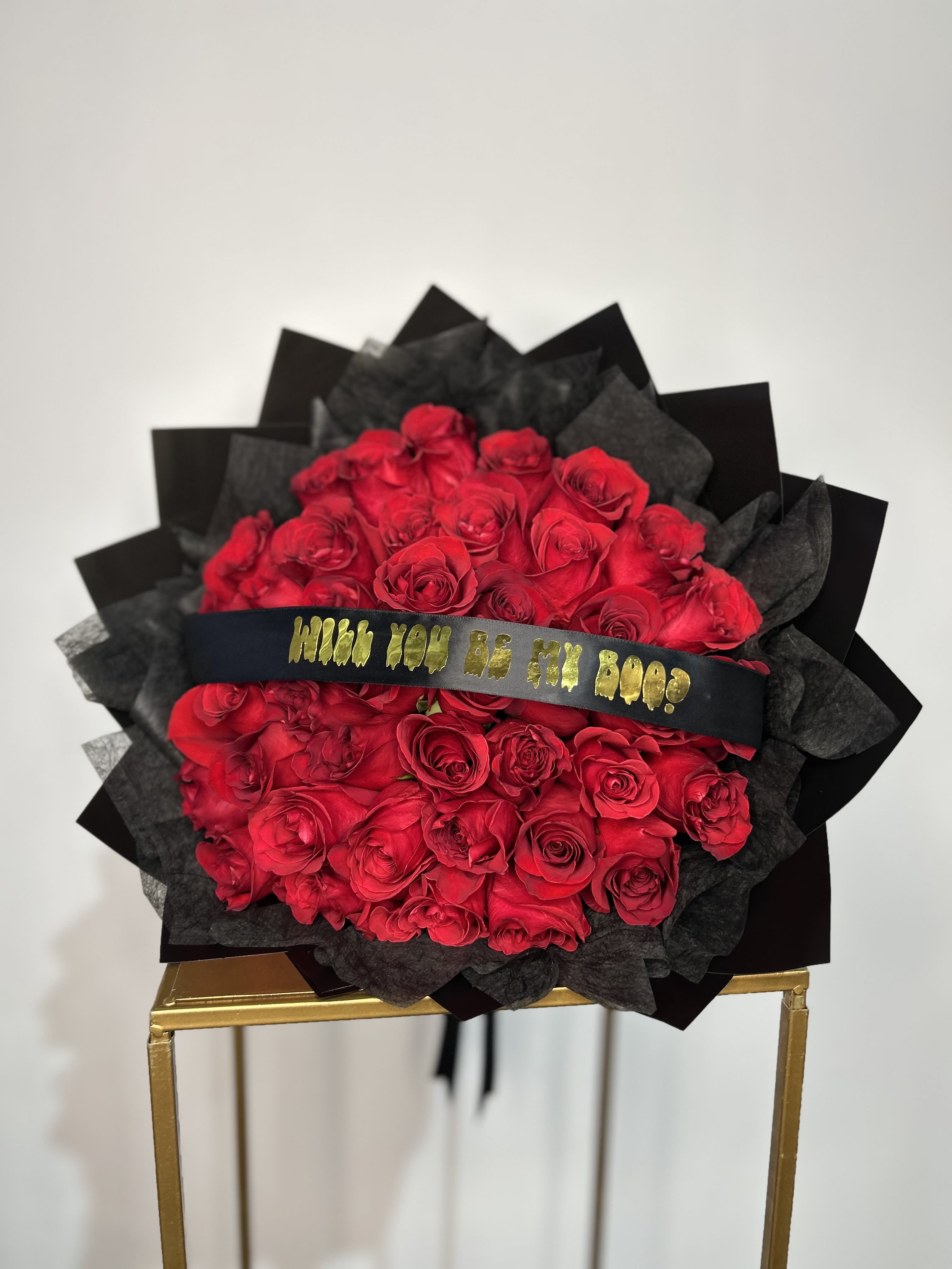 BE MY BOO  - A stunning bouquet of 40 premium red roses, wrapped in sleek black paper and accented with a special golden ribbon engraved with the words “Will You Be My Boo?” A unique, romantic, and playful gift, perfect for surprising someone special this October. Ideal for proposals, anniversaries, or simply showing your love in a stylish and memorable way.   Make your declaration of love unforgettable with this exclusive bouquet.  
