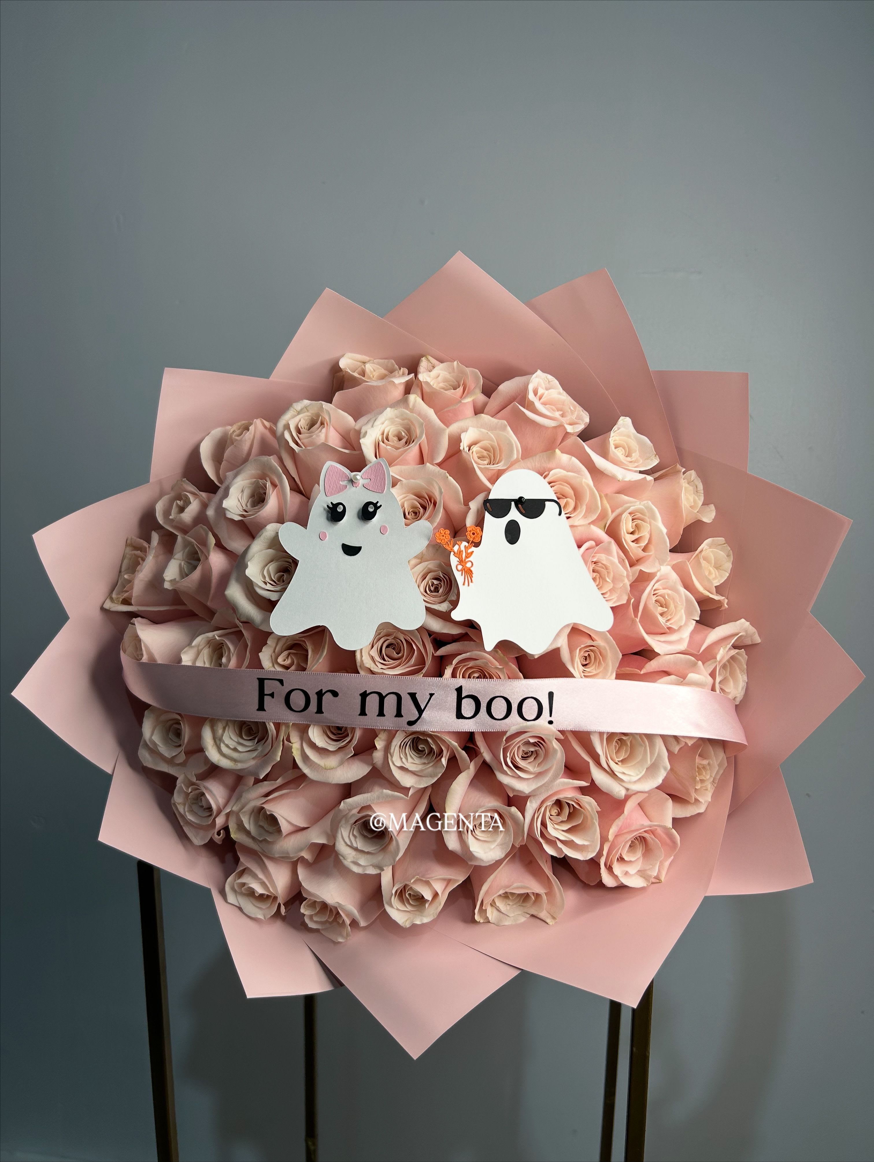 Ghostly Love - Celebrate love with a playful, spooky twist! This charming bouquet features 50 delicate light pink flowers and is accompanied by two adorable ghost figurines—one ghost giving flowers to the other. The bouquet is wrapped elegantly and accented with gold lettering, with the fun message “For My Boo” in black letters.  Perfect for Halloween, October surprises, or just to show someone special that they’re your “boo” in the sweetest way.  A whimsical bouquet that combines romance, charm, and a little spooky fun! 