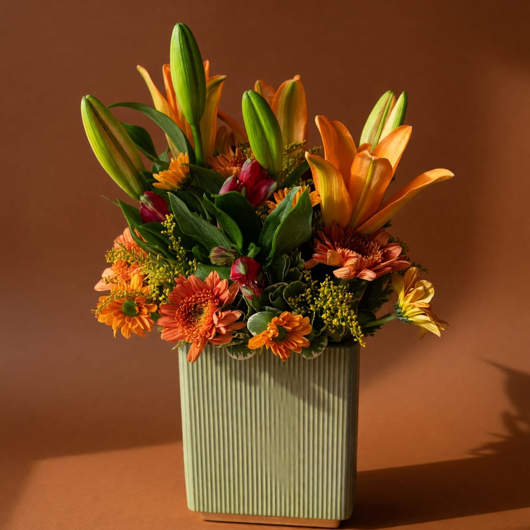Orange lilies and mixed orange flowers in a ribbed rectangular vase