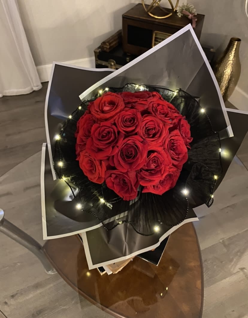 Bouquet of red roses wrapped in black paper with small lights