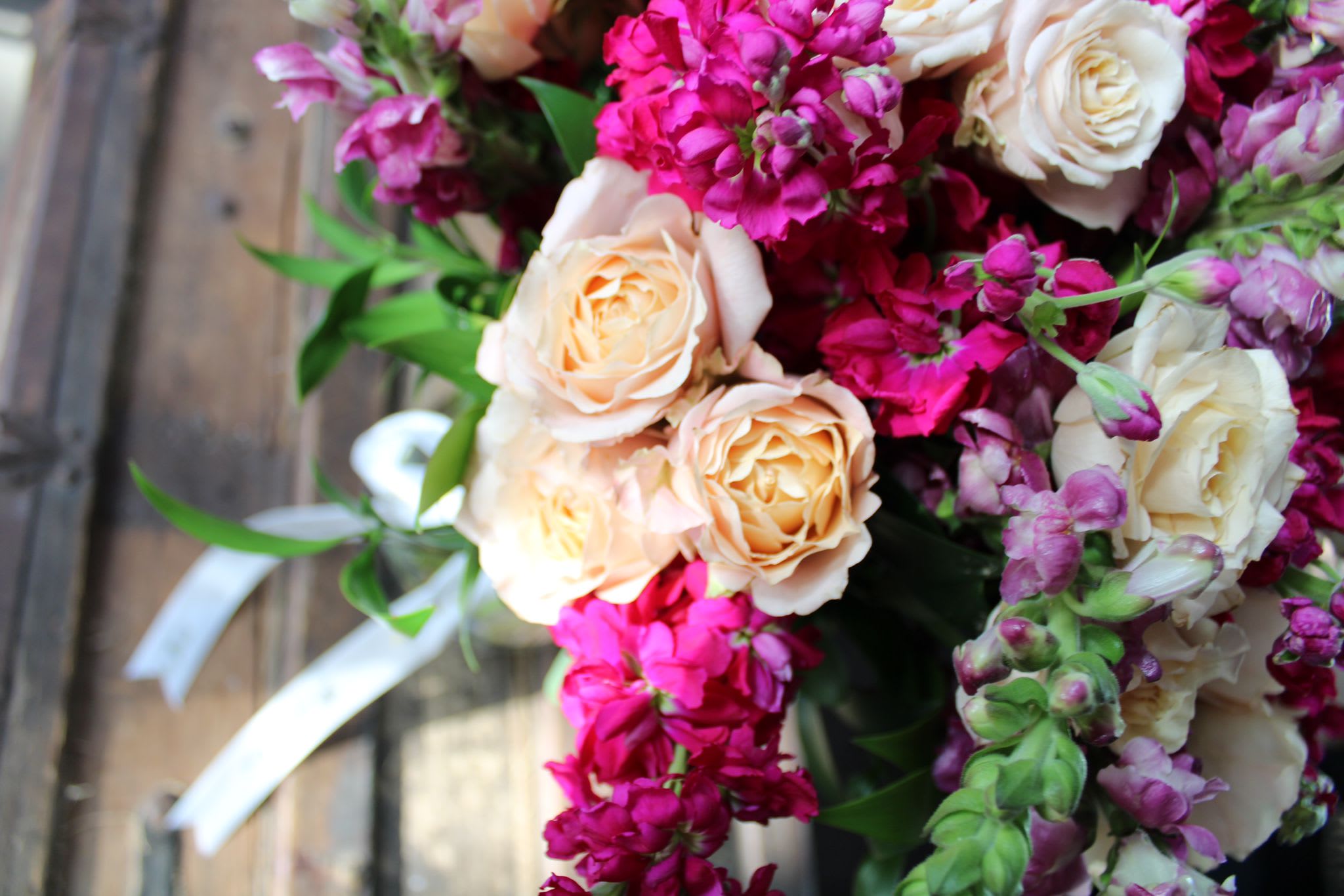 Bouquet of peach roses and magenta flowers with white ribbon