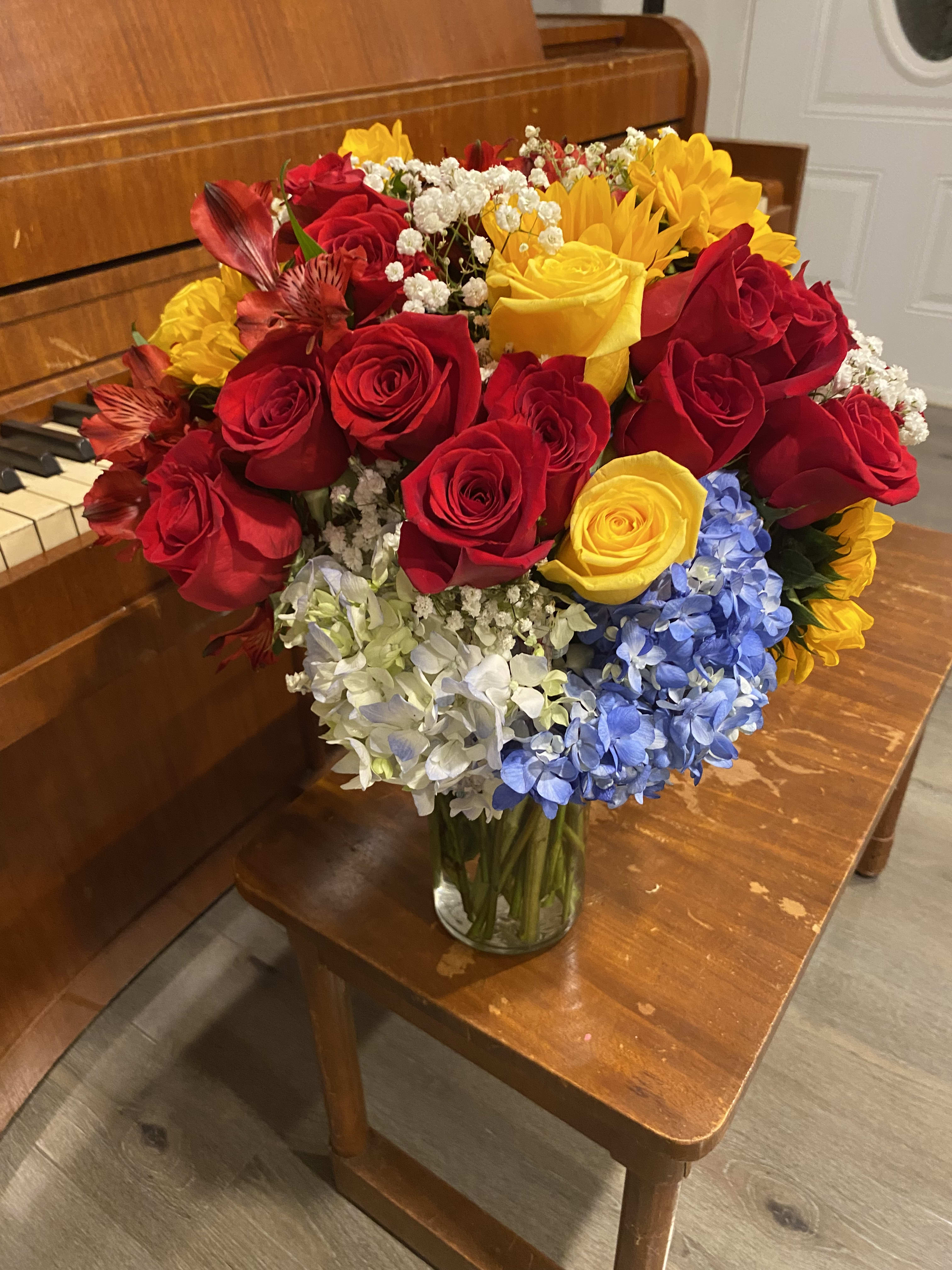 Bouquet of red and yellow roses with blue and white hydrangeas in a glass vase