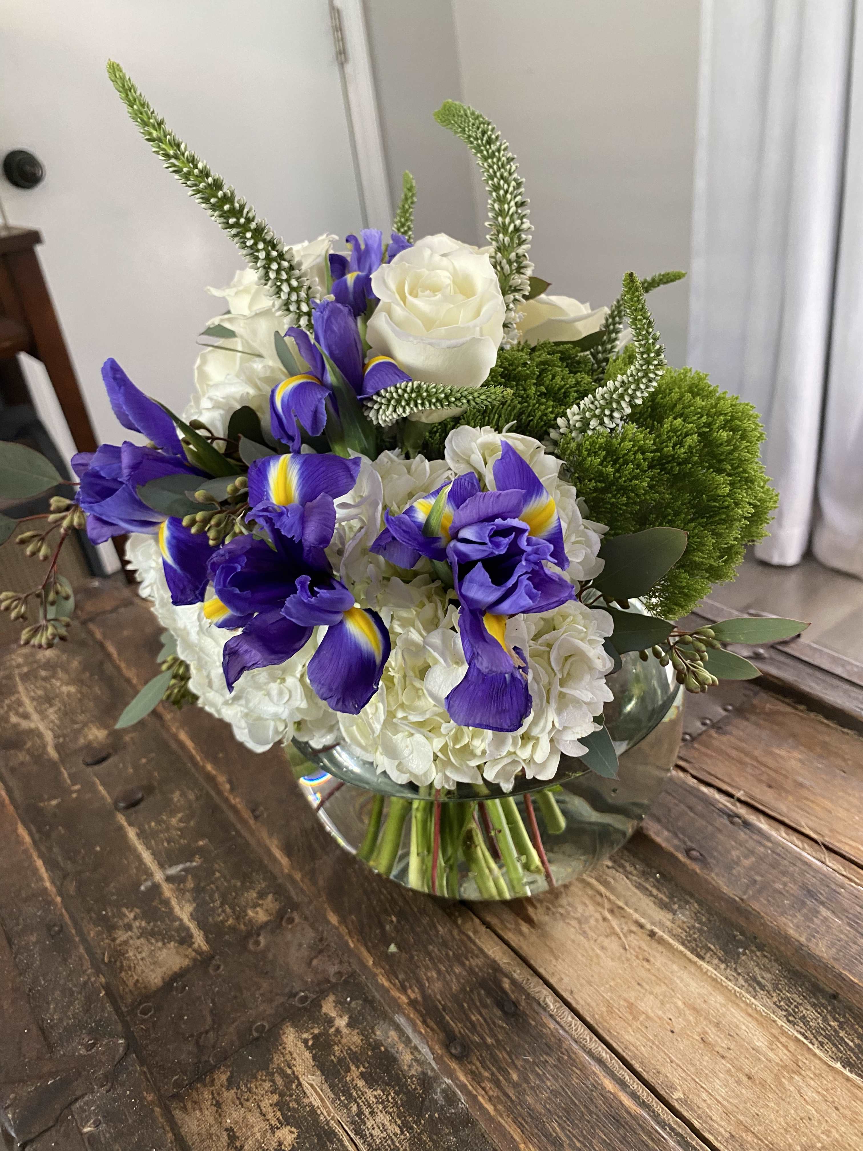 Bouquet of white roses, purple irises, and green accents in a glass vase
