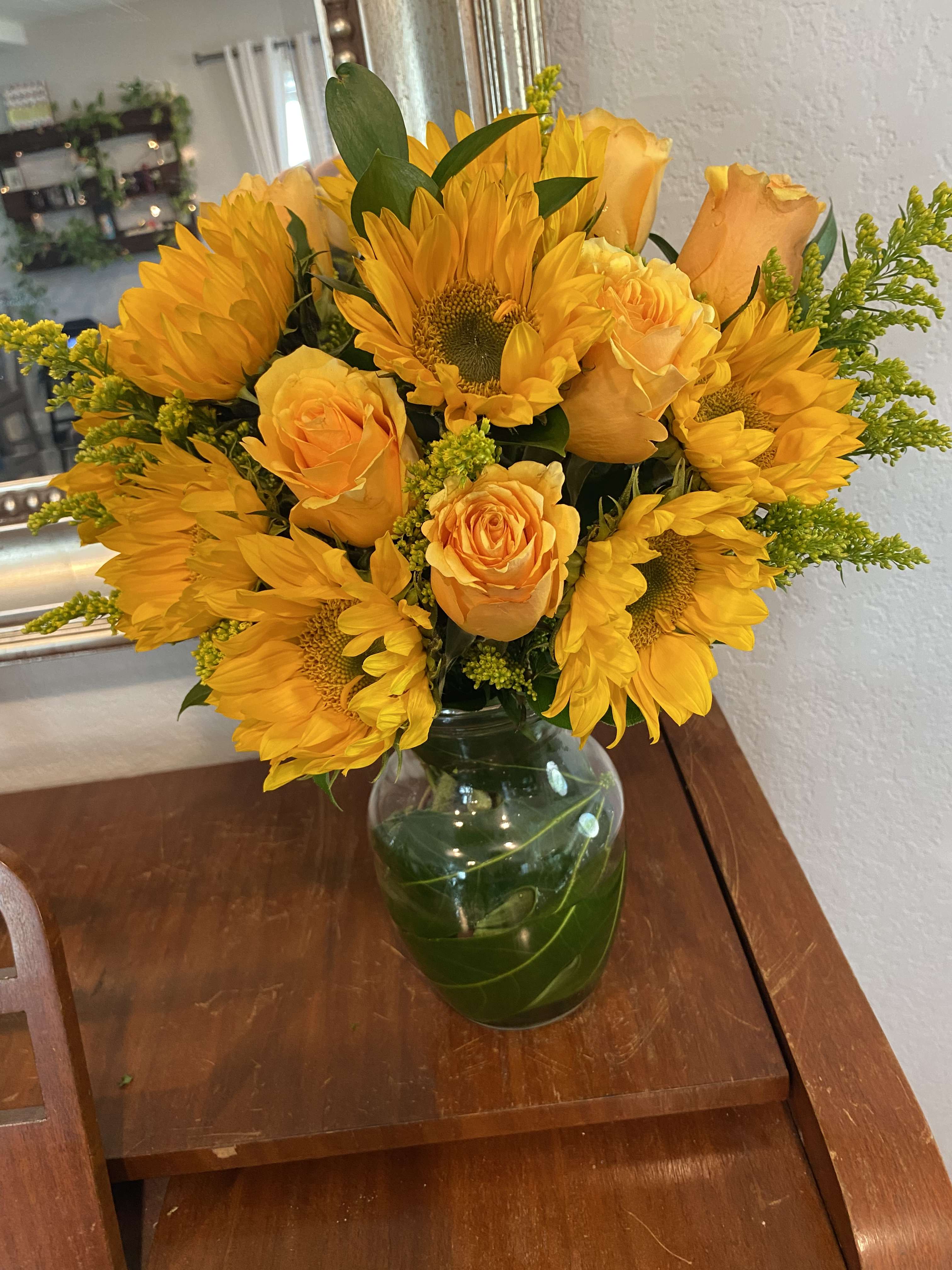 Yellow sunflowers and roses arranged in a glass vase