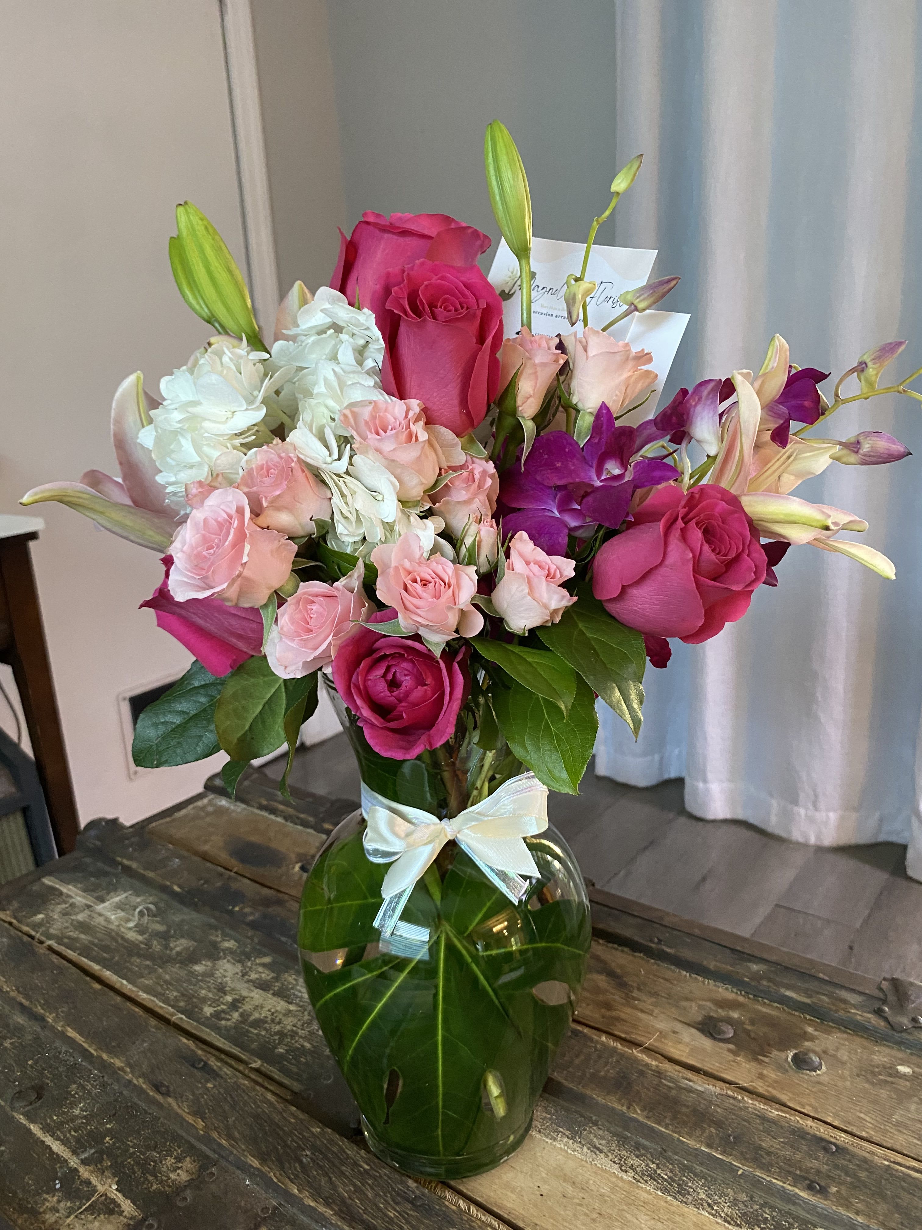 Pink roses and lilies arranged in a glass vase with a ribbon