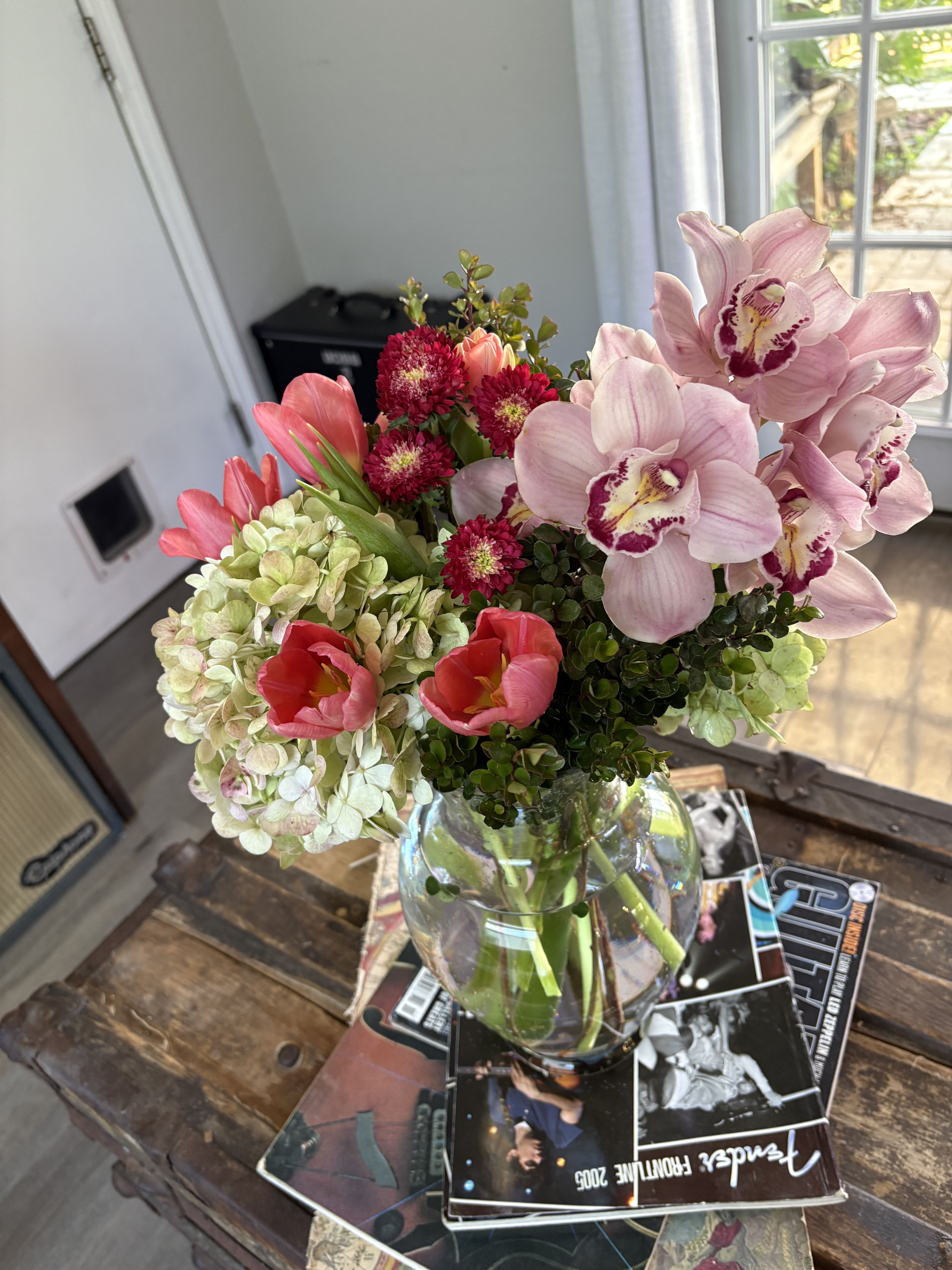 Bouquet of pink orchids, tulips, hydrangeas, and red blooms in a glass vase