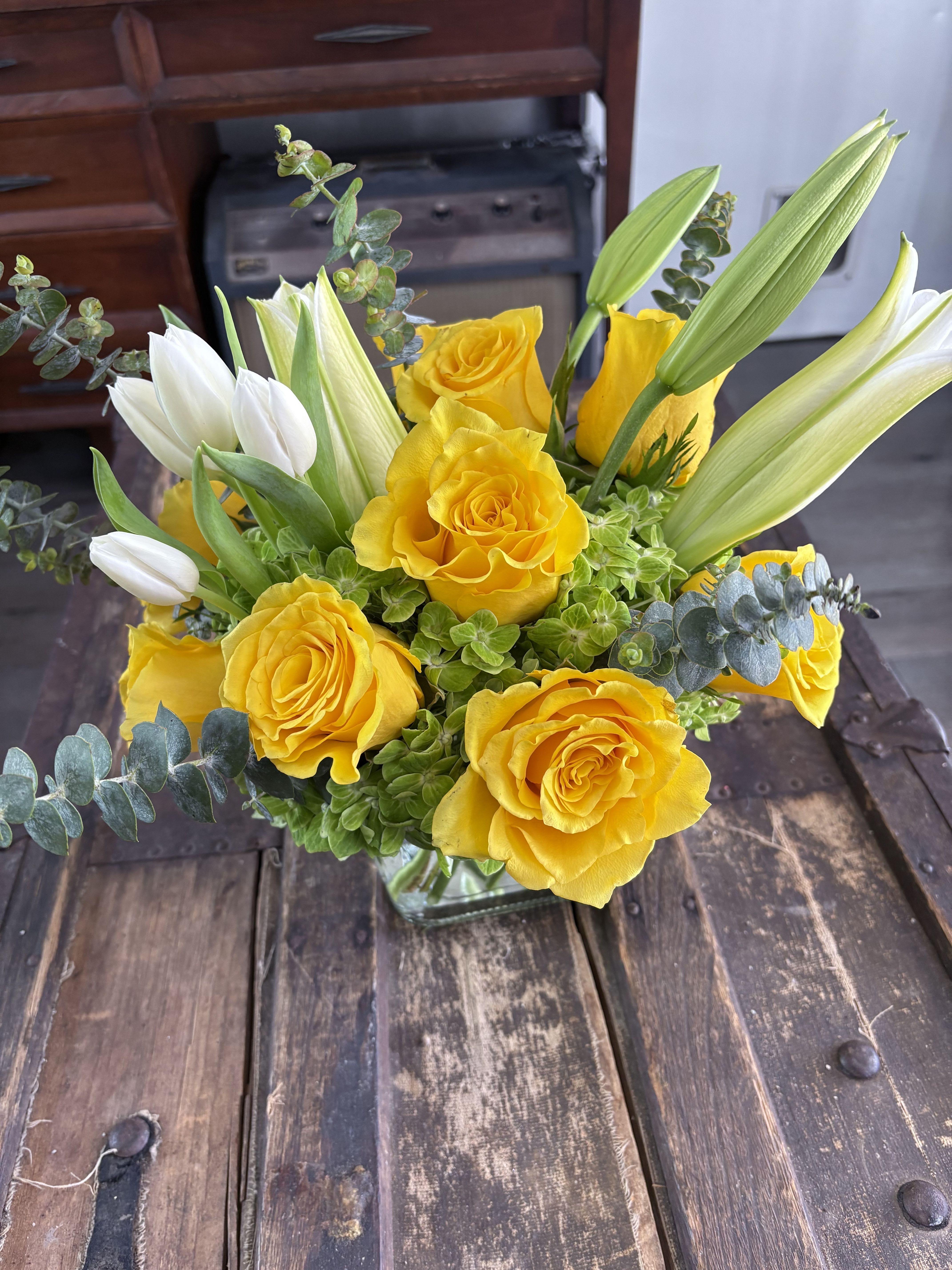 Yellow roses and white tulips arranged in a glass vase