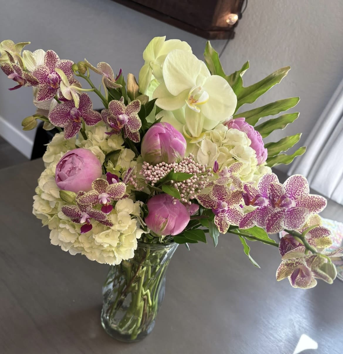 Bouquet of pink peonies, white hydrangeas, and spotted orchids in a glass vase