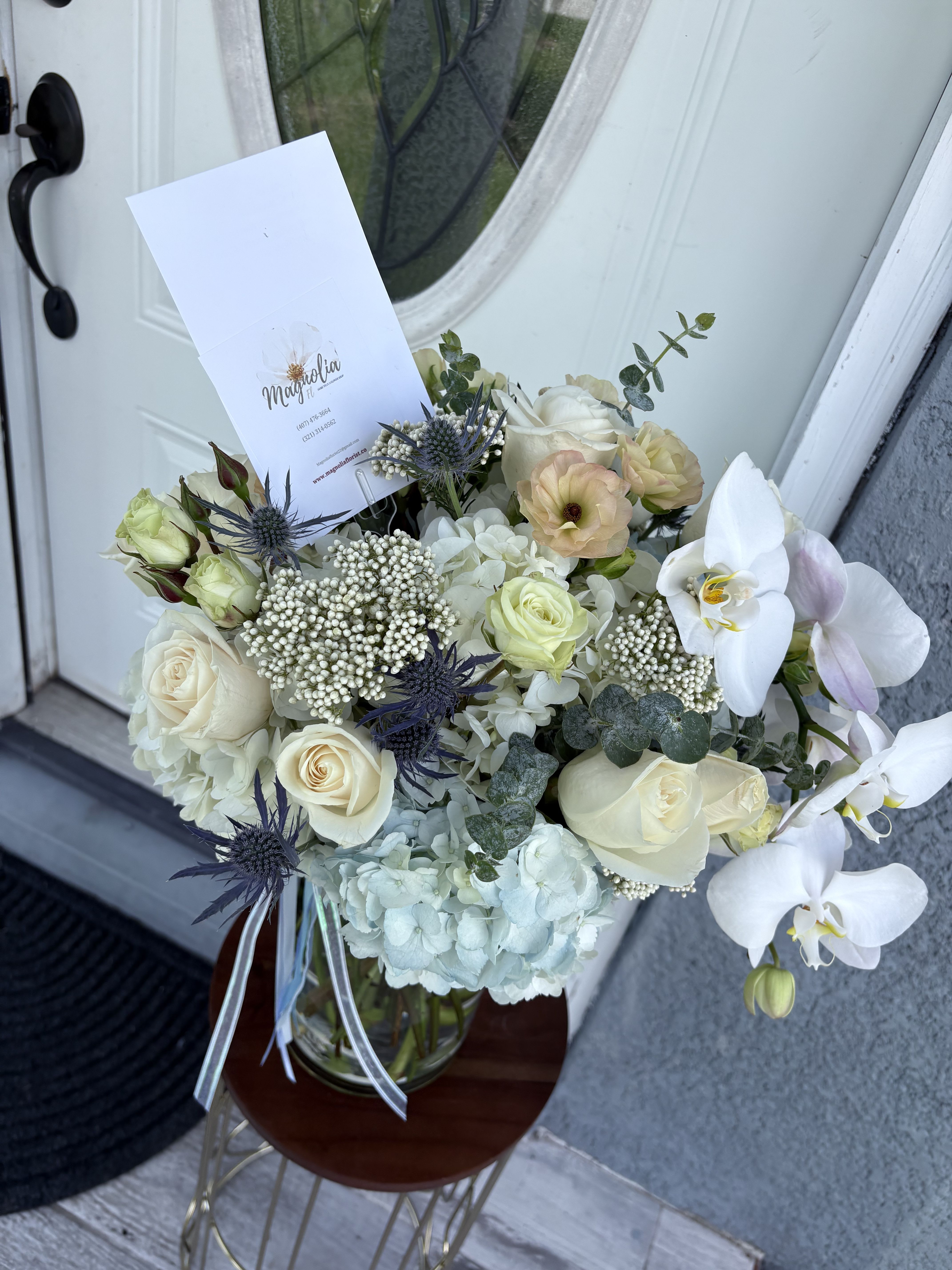 Bouquet of white roses, orchids, and pale hydrangeas in a glass vase