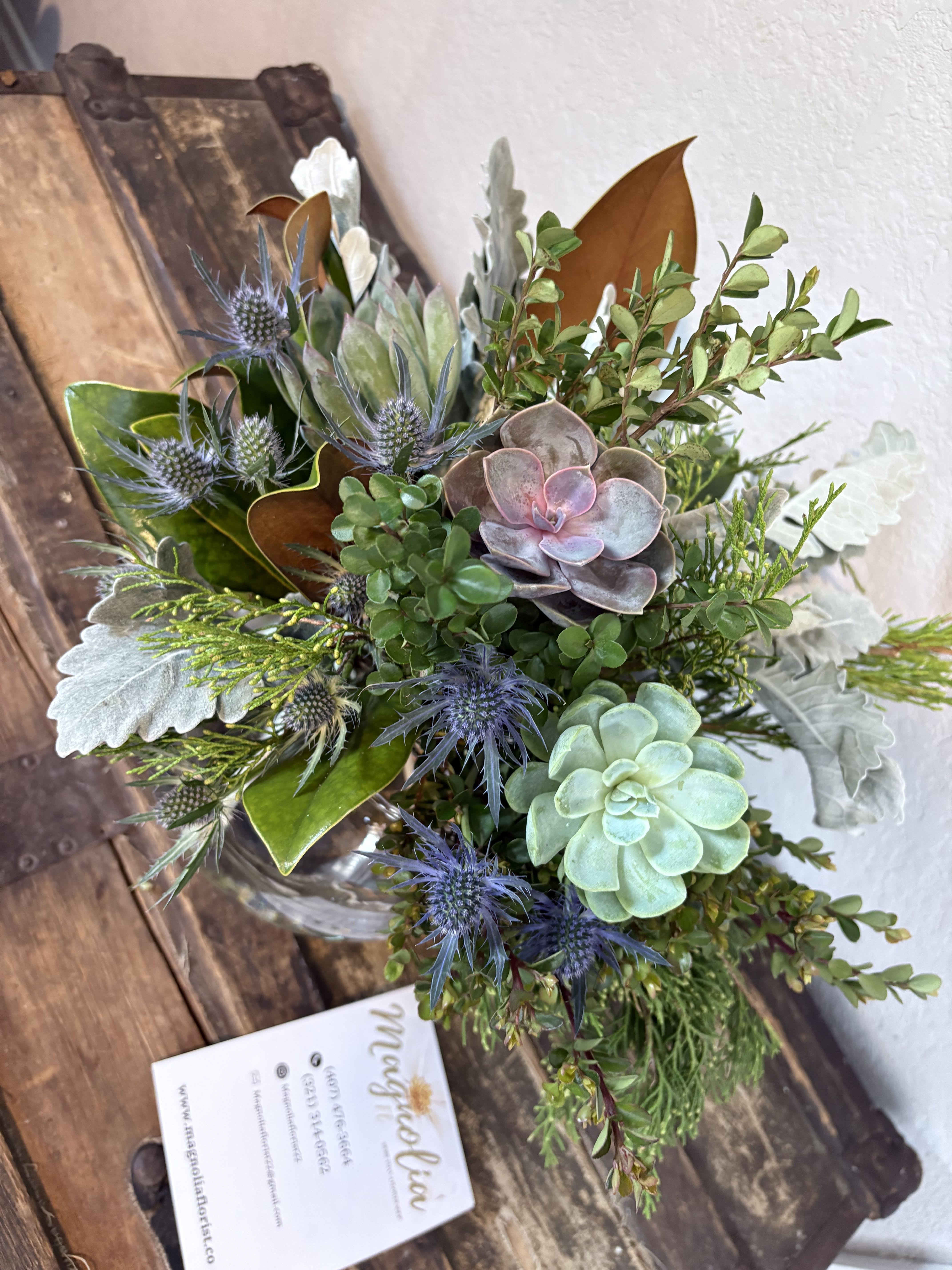 Succulent arrangement with blue thistle-like blooms in a glass vase