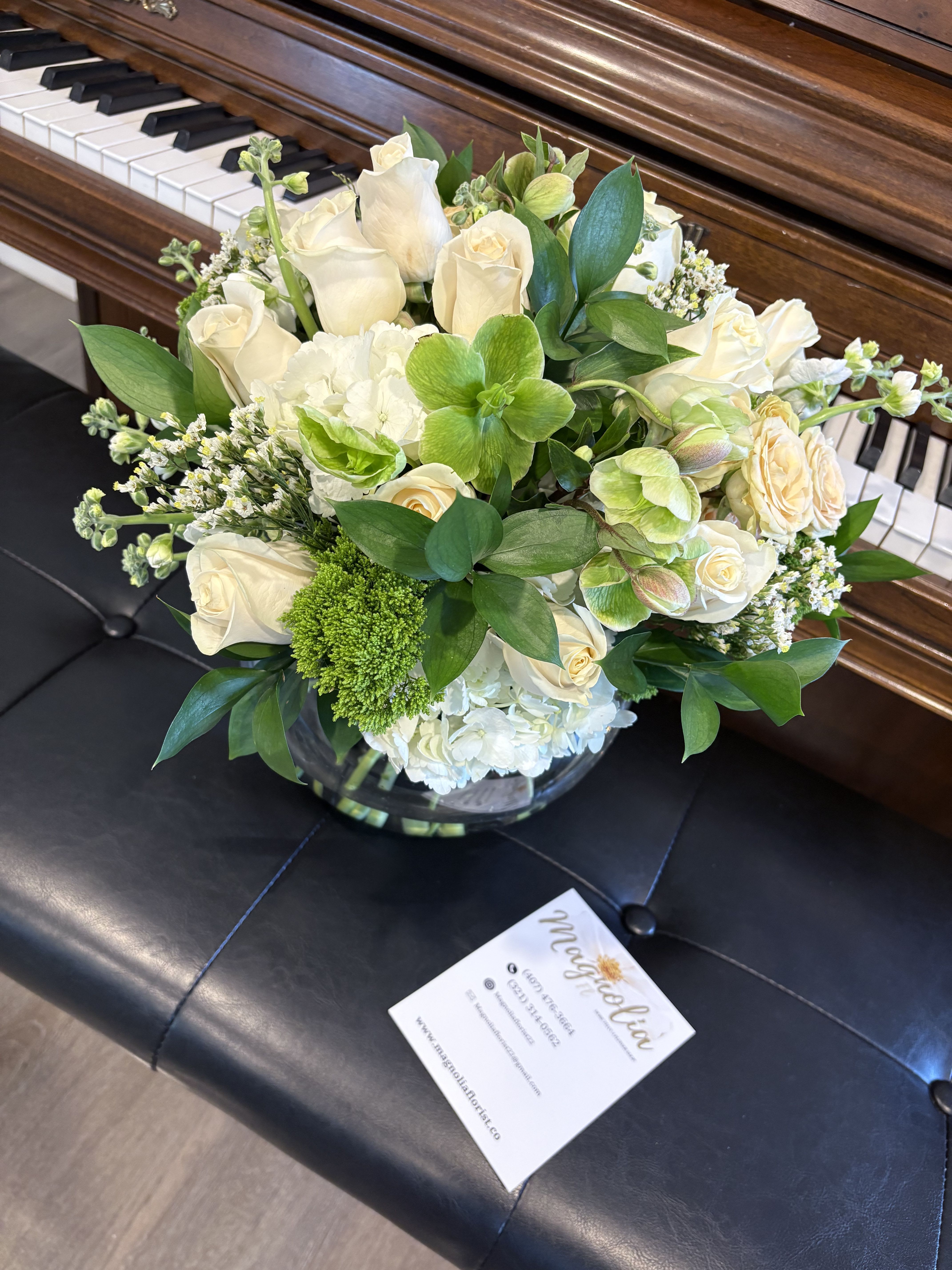 White rose and green floral arrangement in a glass vase on a piano bench