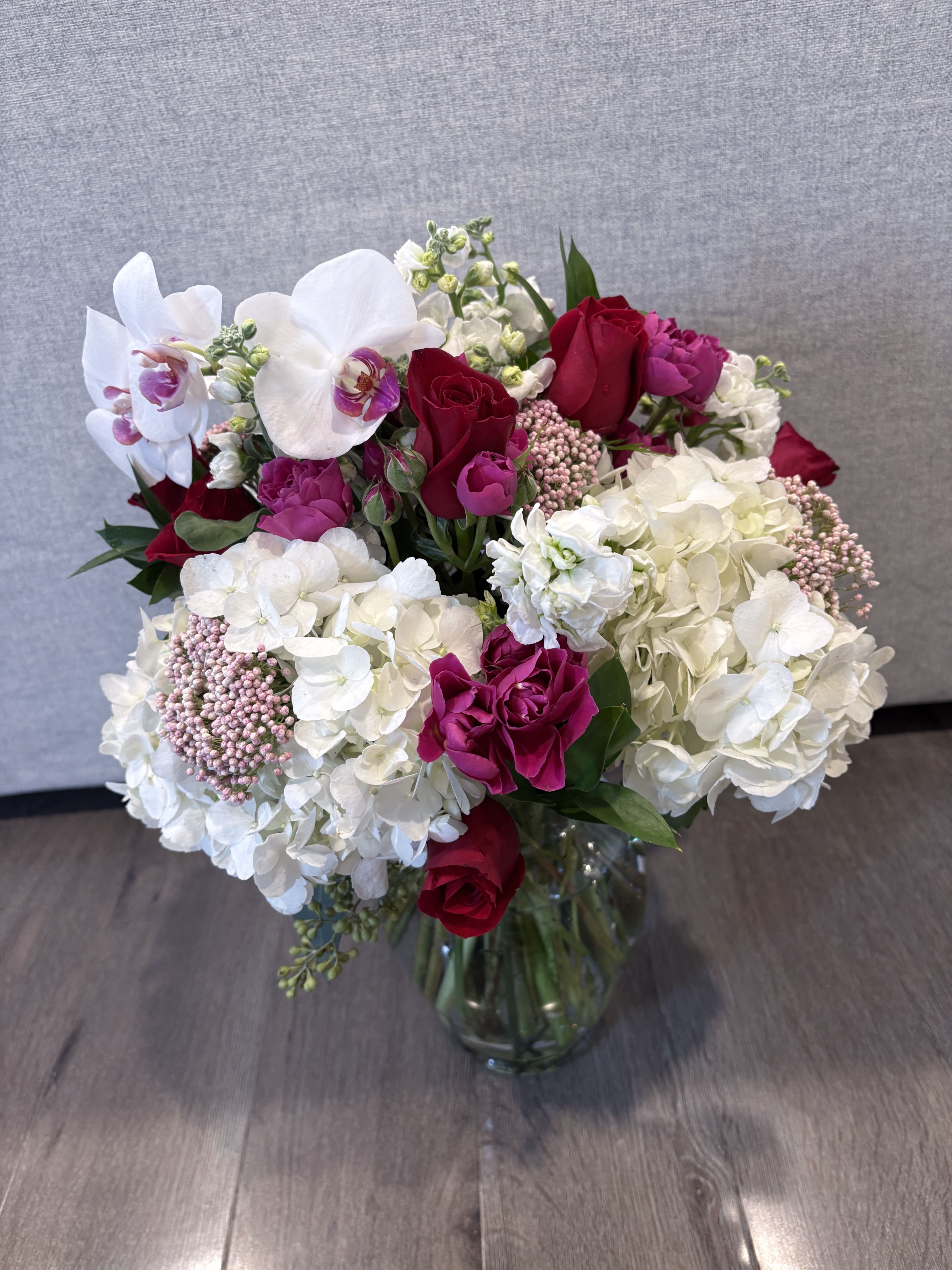 Bouquet of red roses, white orchids, and white hydrangeas in a glass vase
