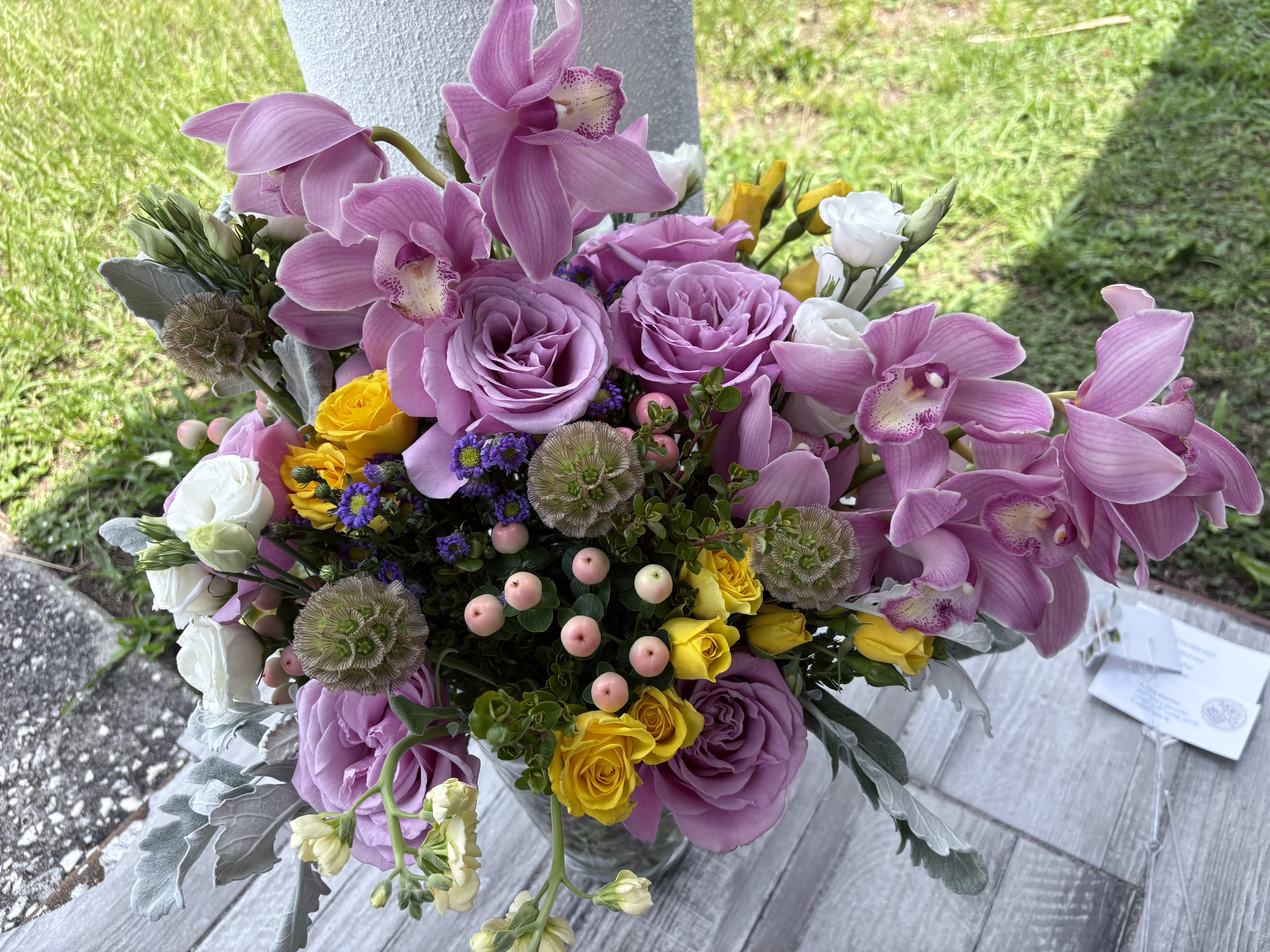Bouquet of pink orchids, lavender roses, and yellow spray roses in a vase