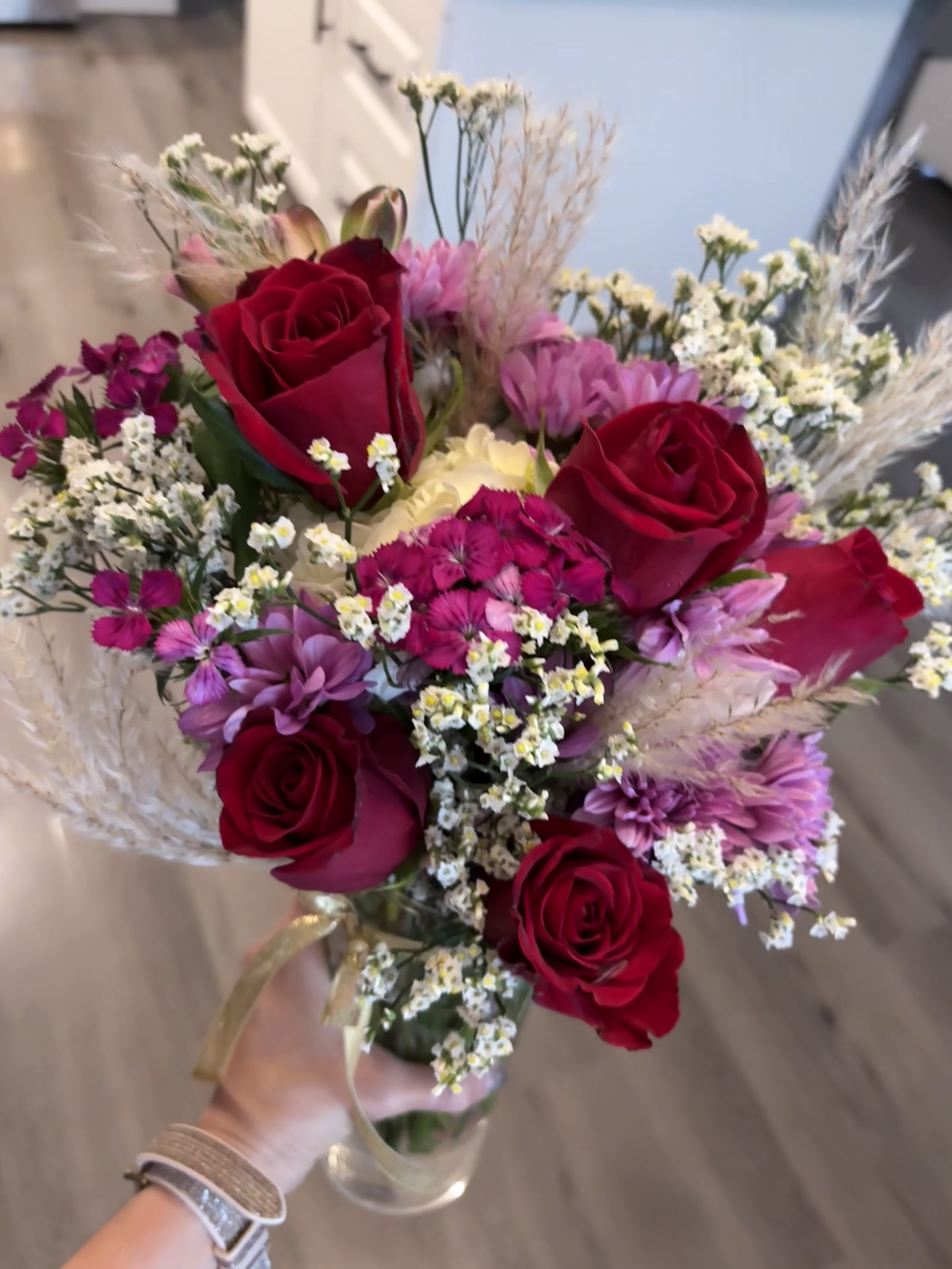 Handheld bouquet of red roses and pink-purple flowers in a clear vase