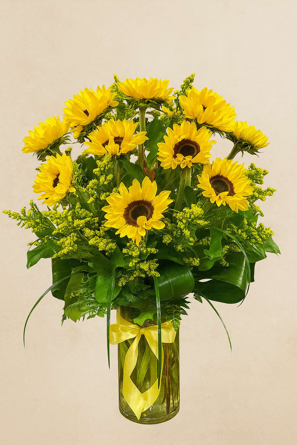 Golden Radiance - A celebration of pure joy, our Golden Radiance arrangement brings the warmth of the countryside into the elegance of your home. Luminous sunflowers are artfully gathered with verdant seasonal foliage and golden accents, creating a display that is both cheerful and refined. Presented in a clear glass cylinder, finished with a hand-tied satin ribbon, this bouquet captures the effortless sophistication that is the hallmark of Savington &amp; Hill. Perfect for brightening a sunlit breakfast table or gifting with heartfelt warmth, Golden Radiance is a timeless expression of happiness, crafted with heritage and grace.