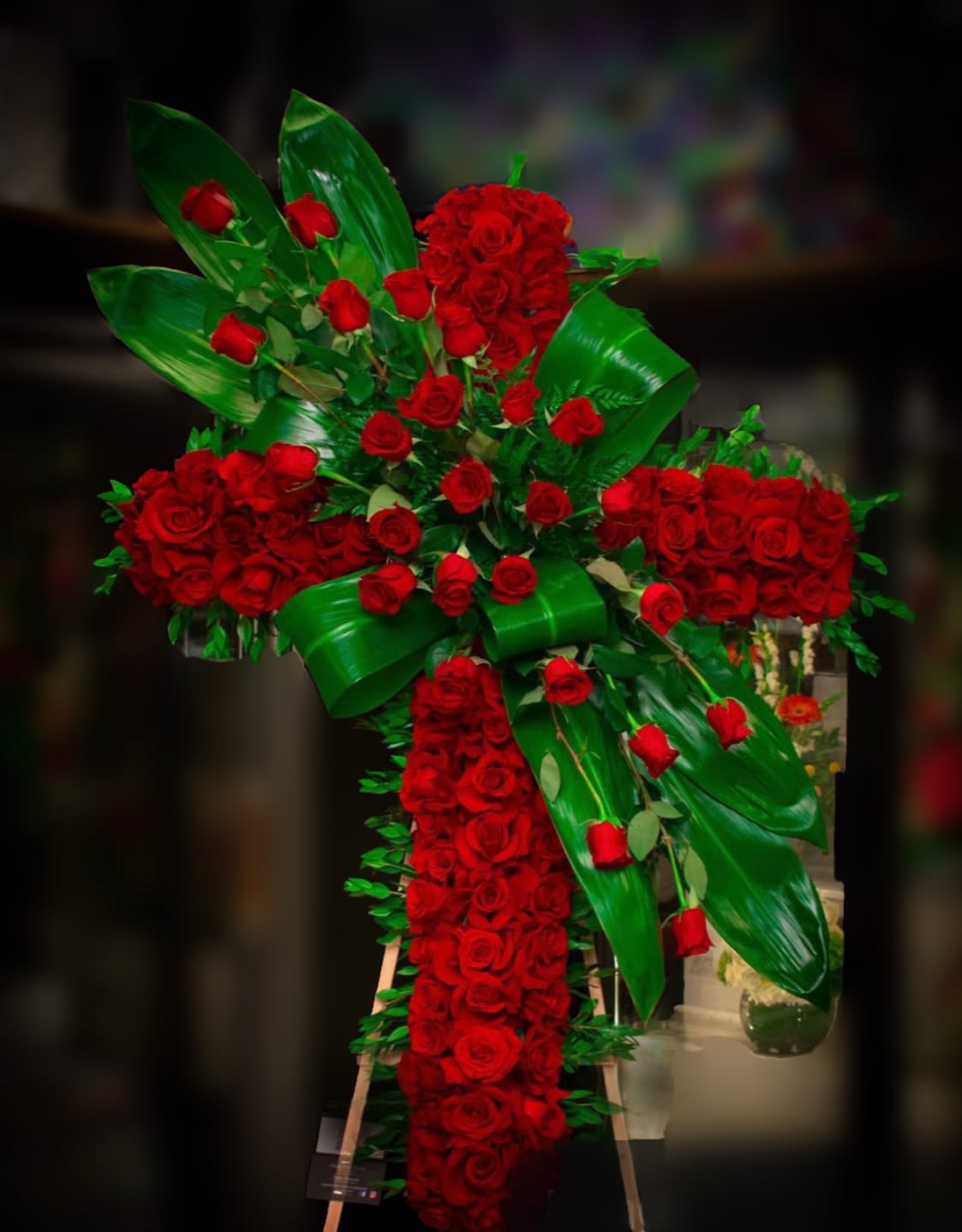 Large cross-shaped arrangement of red roses with glossy green leaves
