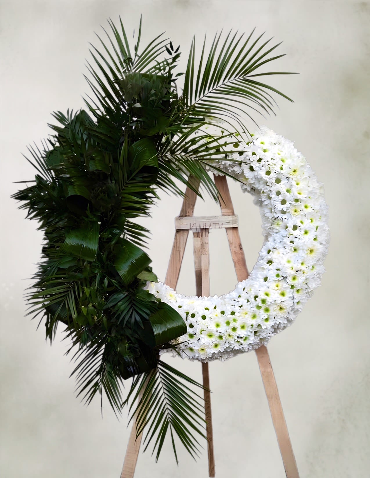 Large floral wreath with white flowers and dark palm fronds on an easel