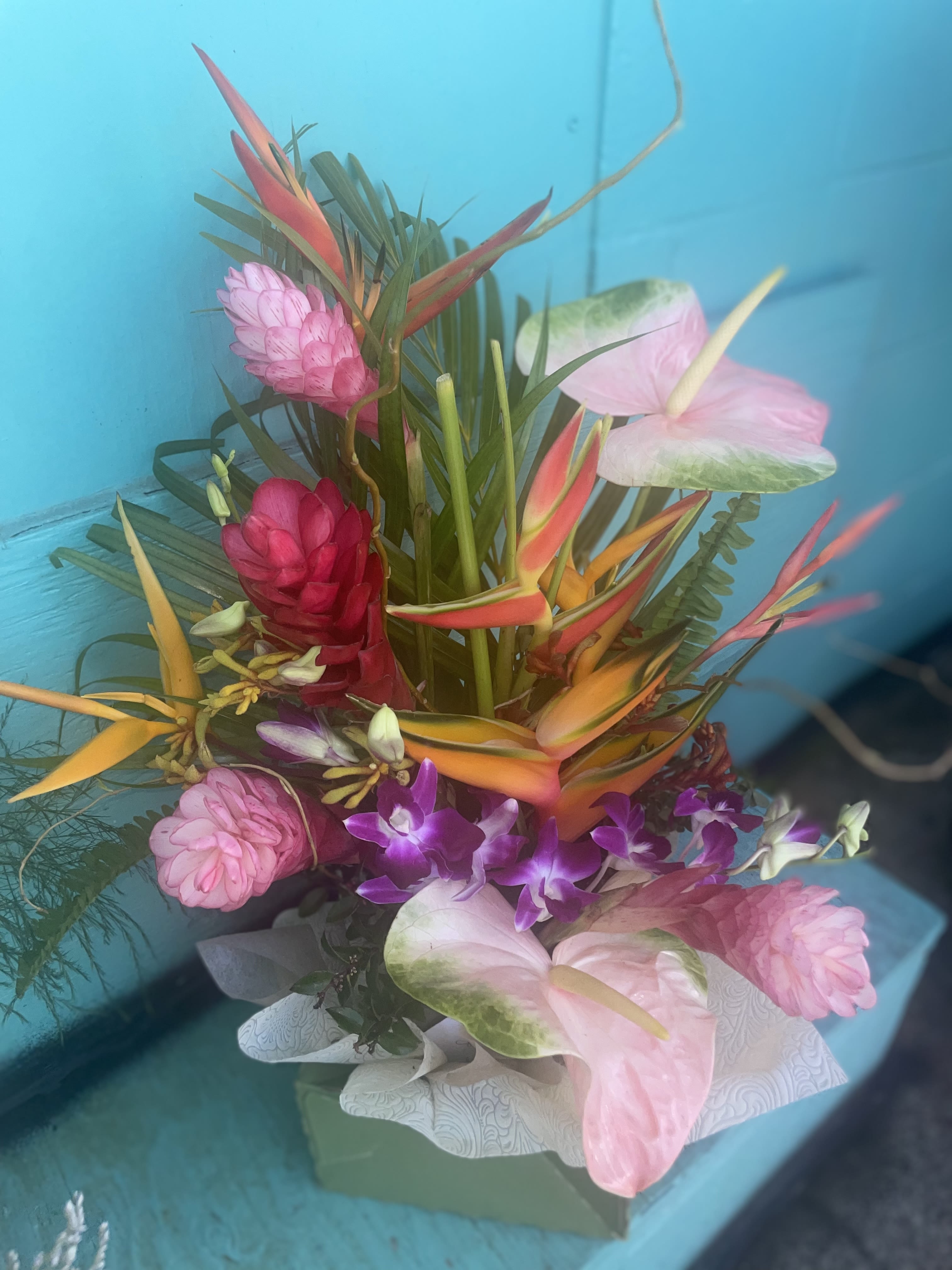 Tropic Like It's Hot by BloomNation™ - Tropical plants come together in this one-sided tall standing arrangement. Featuring birds of paradise, ginger, and pincushion protea, this tropical selection would look lovely in any home. Tropicals depend on availability and will Be substituted accordingly . Mahalo   Approximate Dimensions: 22"D x 30"H