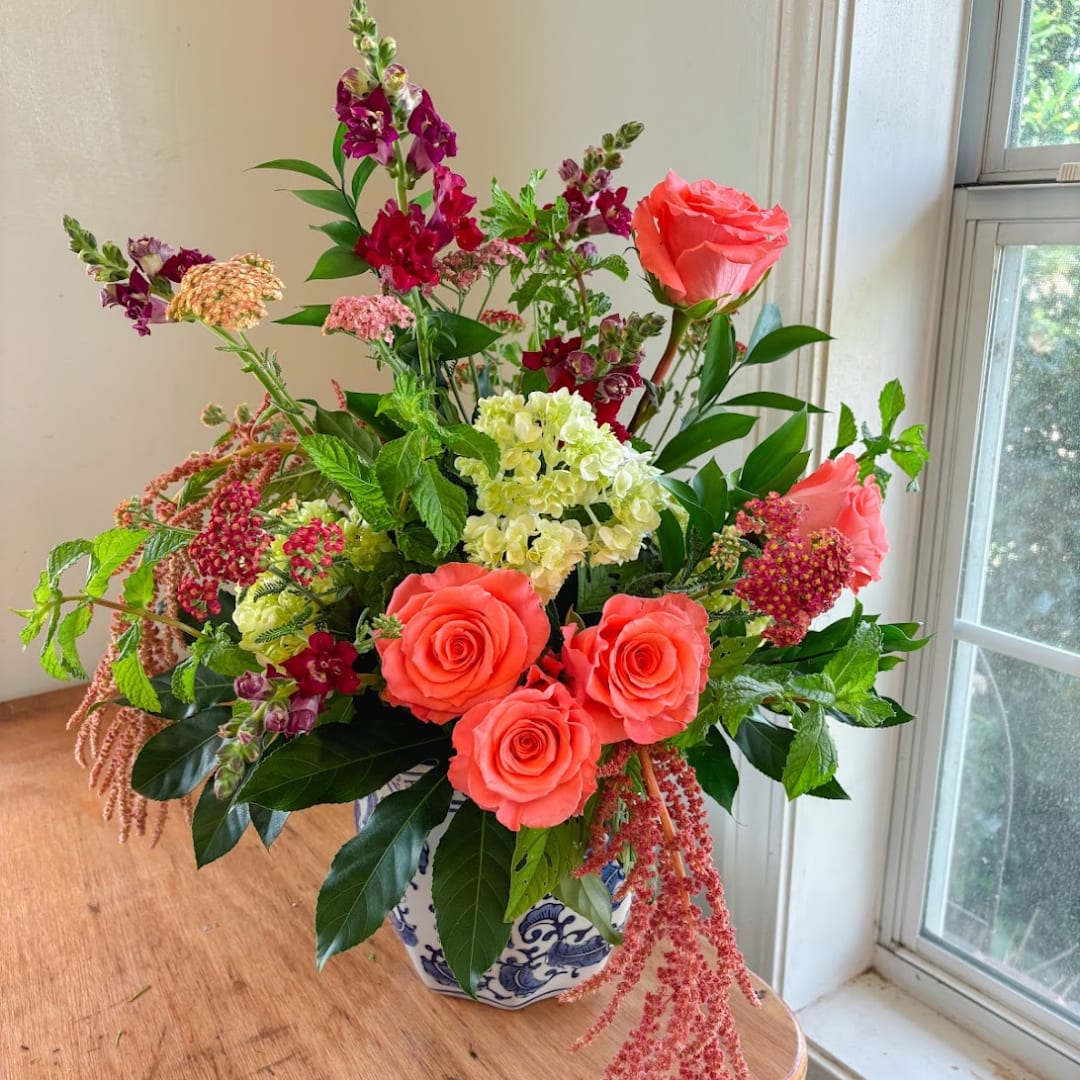 Mixed bouquet with coral roses, hydrangea, and snapdragons in a blue-and-white vase