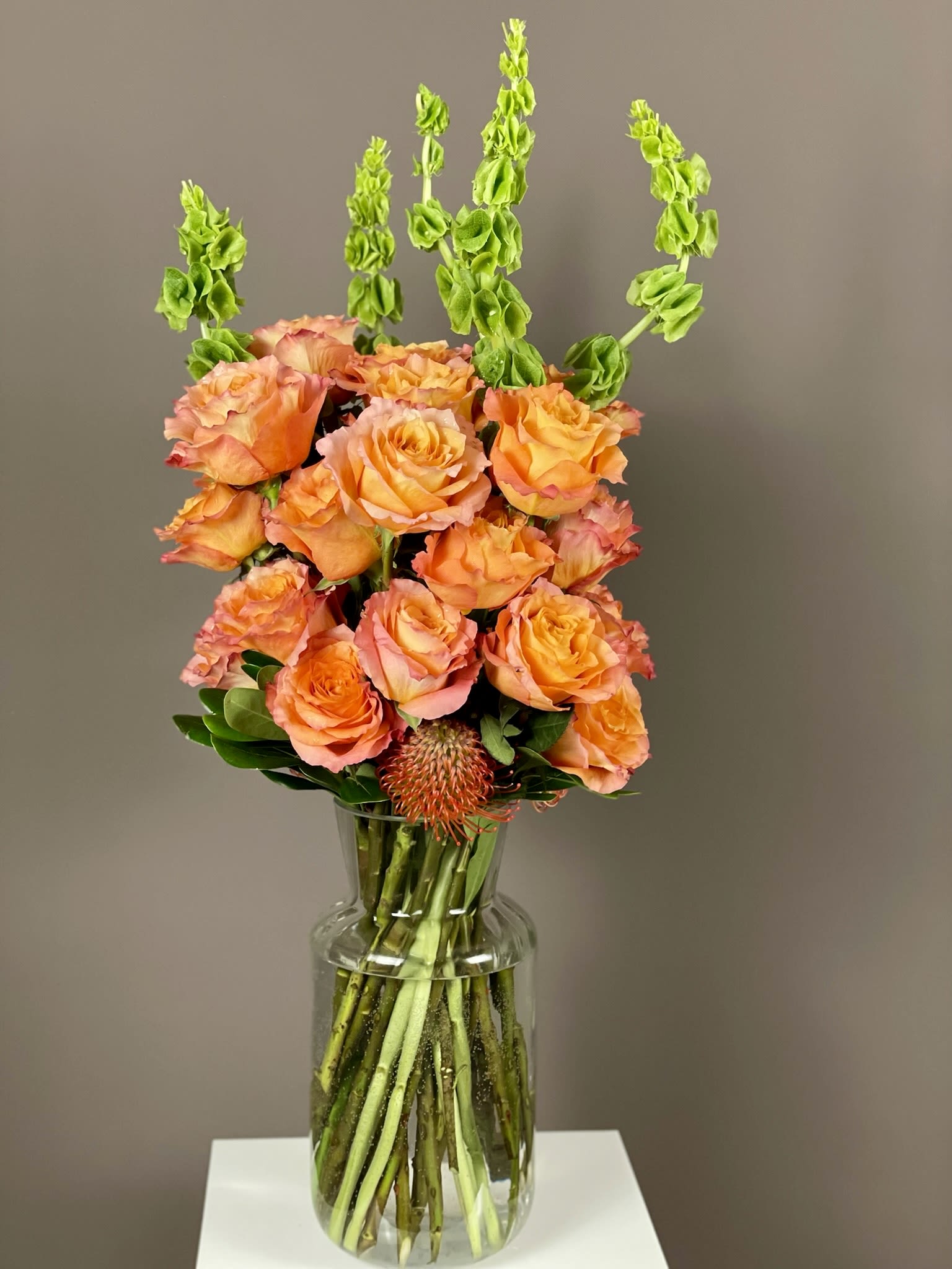 Orange roses in a clear glass vase with tall green spikes