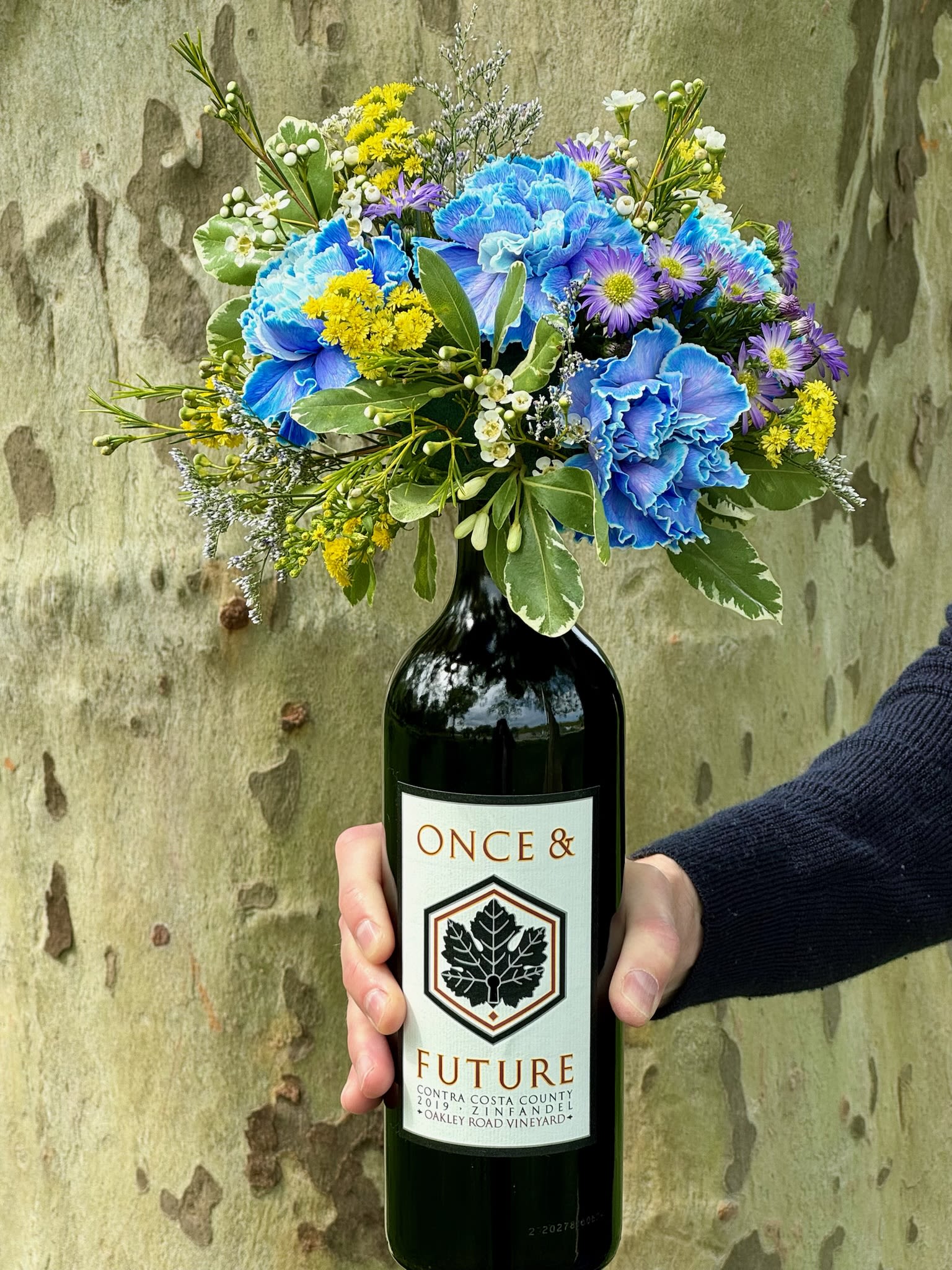 Bouquet of blue, purple, and yellow flowers in a wine bottle vase