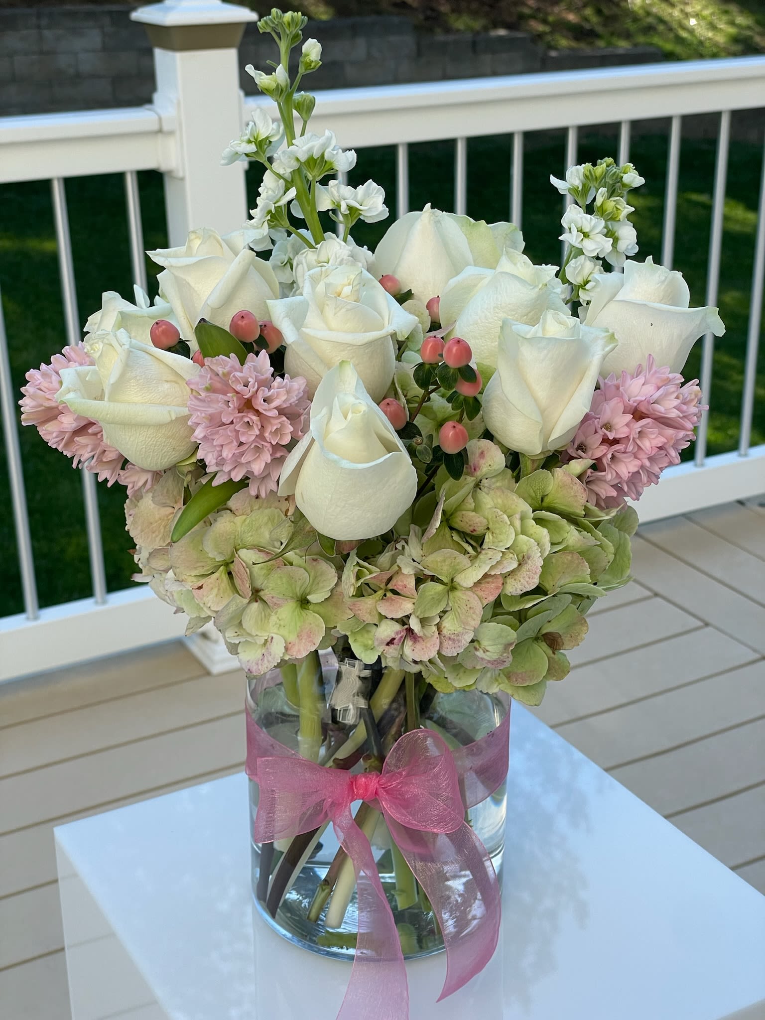 White roses and pink flowers arranged in a glass vase with a pink ribbon