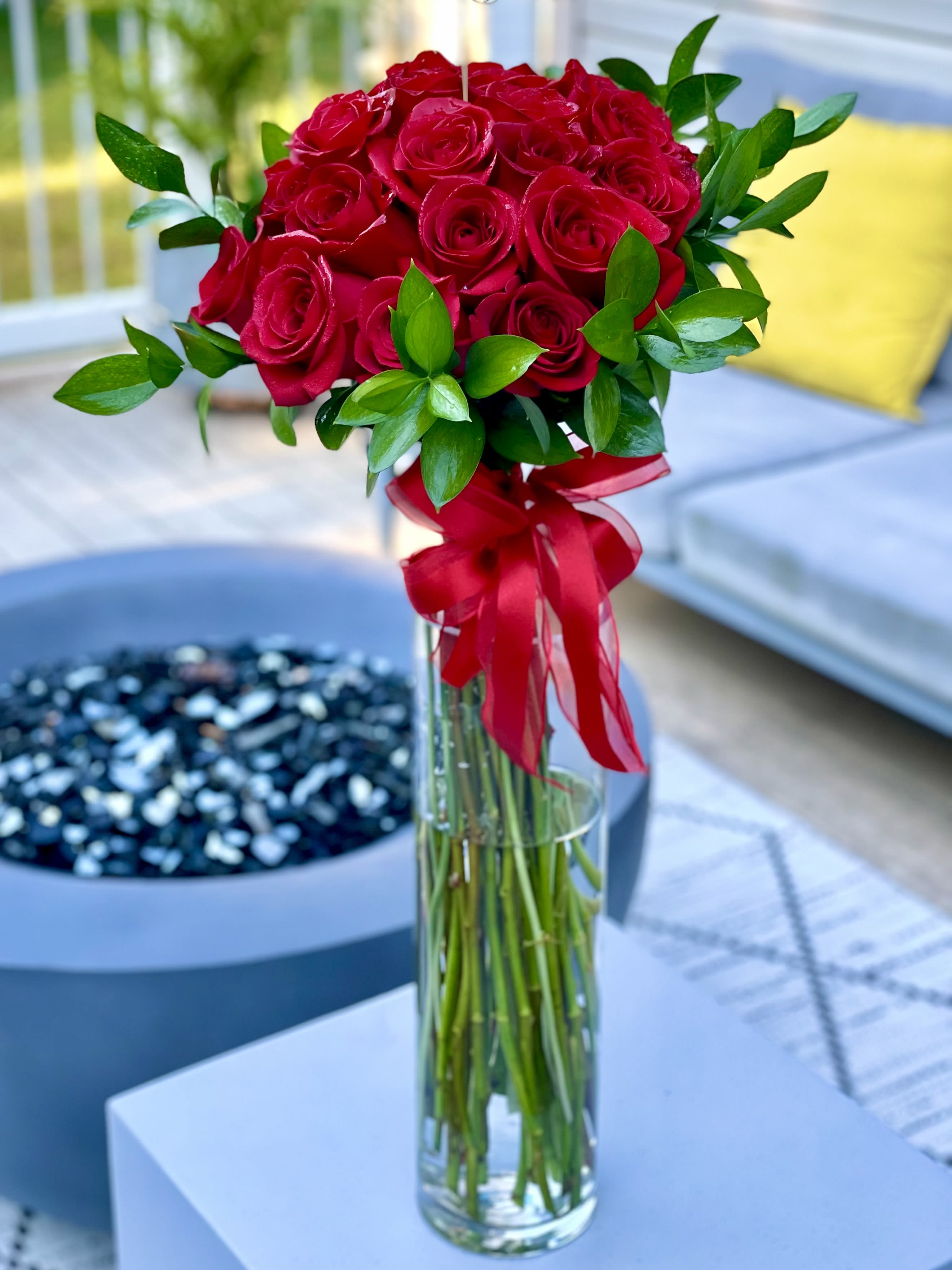 Red rose bouquet in a tall glass vase with a red ribbon