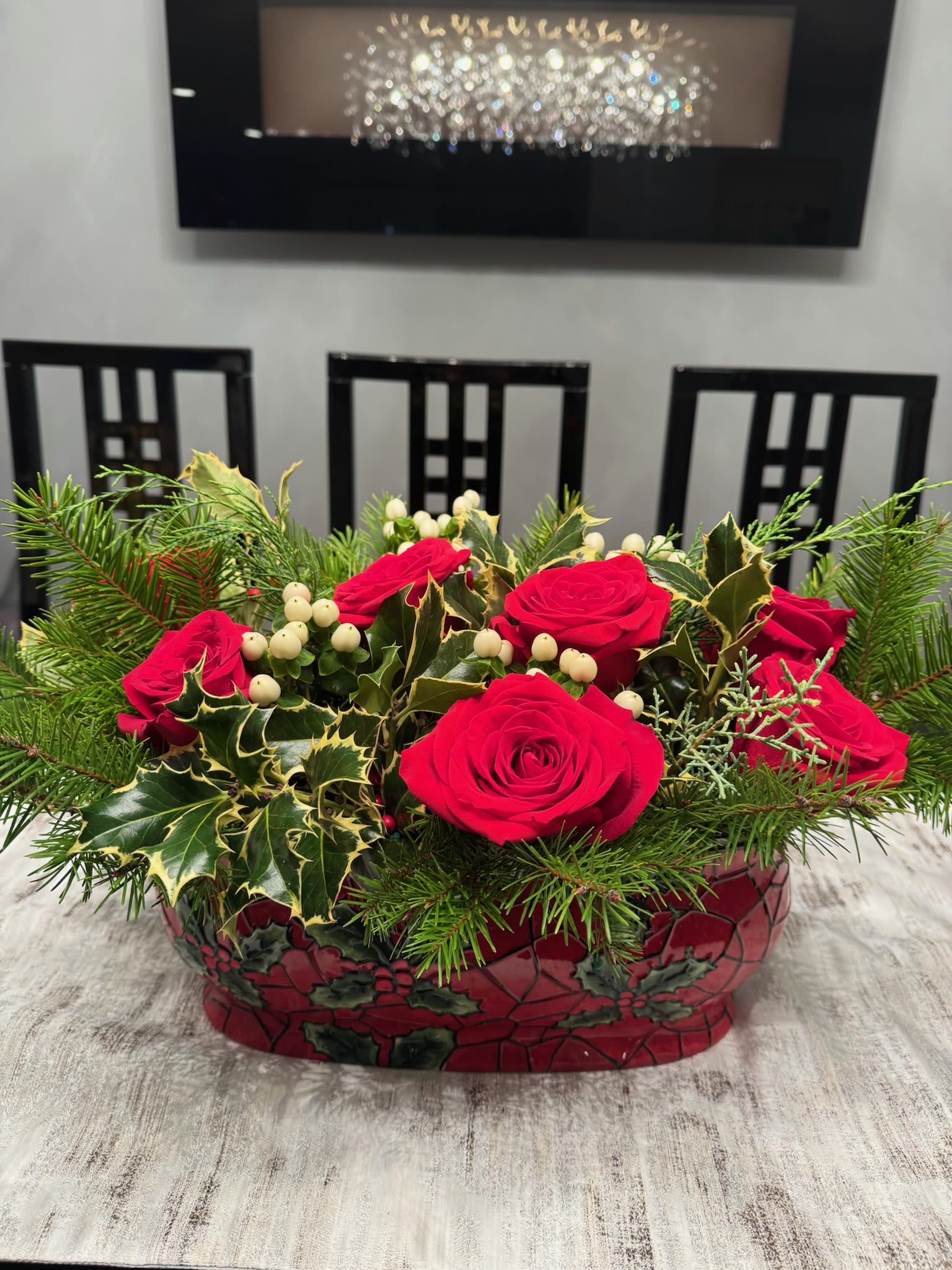 Red roses in a decorative holiday container with evergreen and berry accents