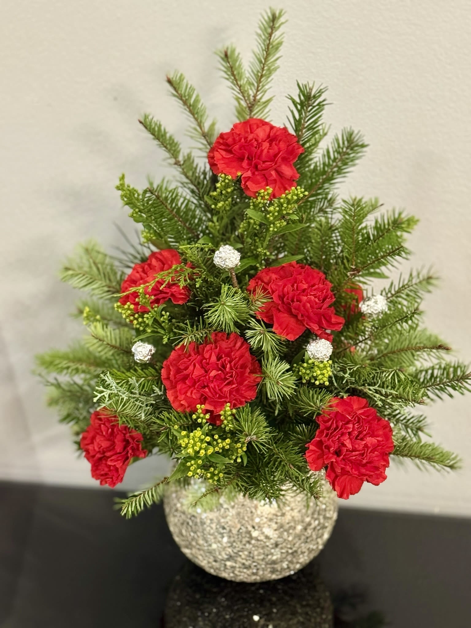 Red carnations in a glittery round vase with evergreen sprigs