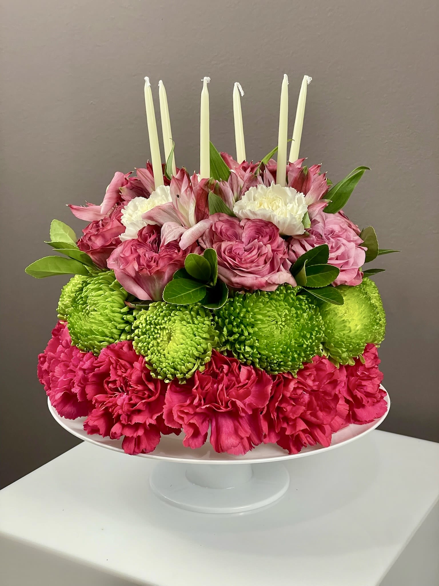 Pink and green floral centerpiece with white candles on a pedestal stand