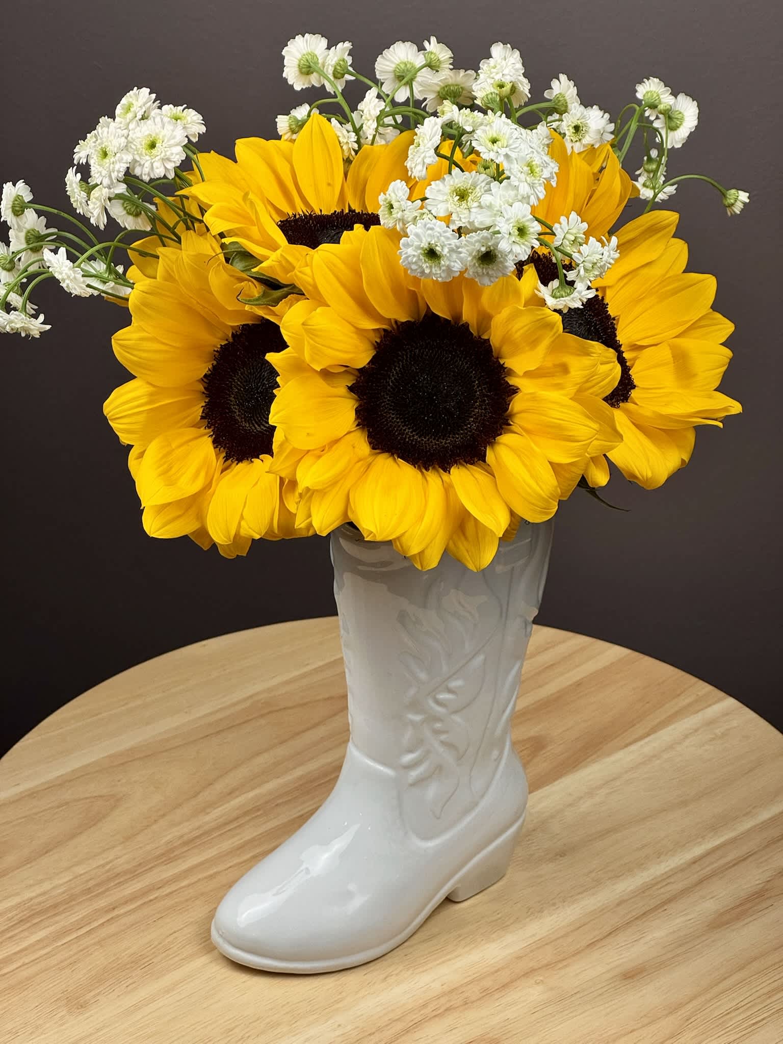 Sunflowers and white daisy-like flowers arranged in a white boot vase