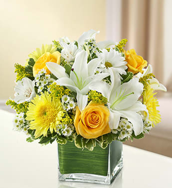 Yellow roses and white lilies in a square glass vase