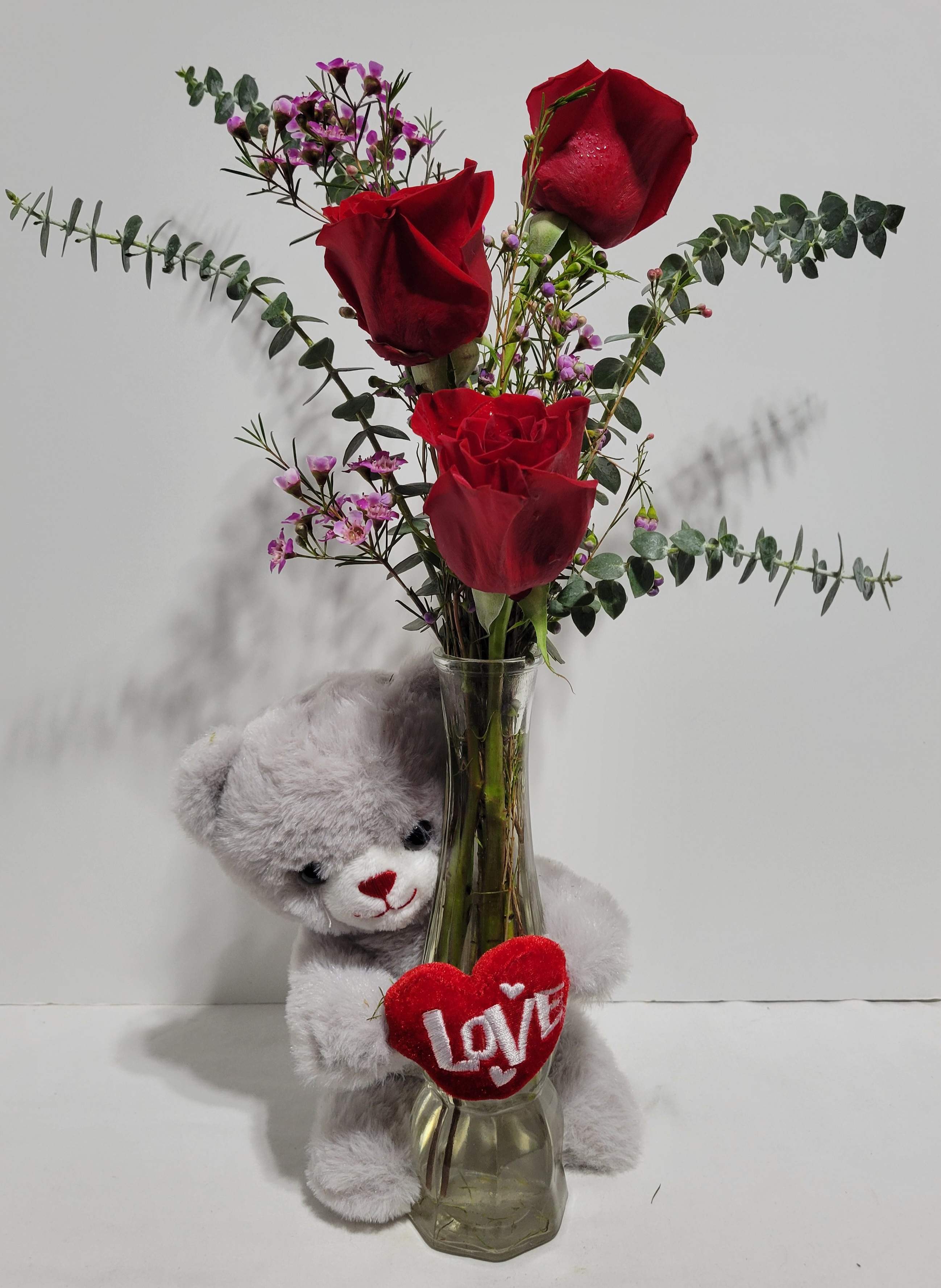 Red roses in a glass vase with a teddy bear and heart decoration
