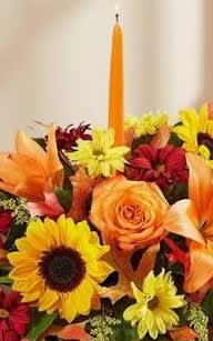 Colorful flower arrangement with sunflowers, roses, and lilies around a tall orange candle