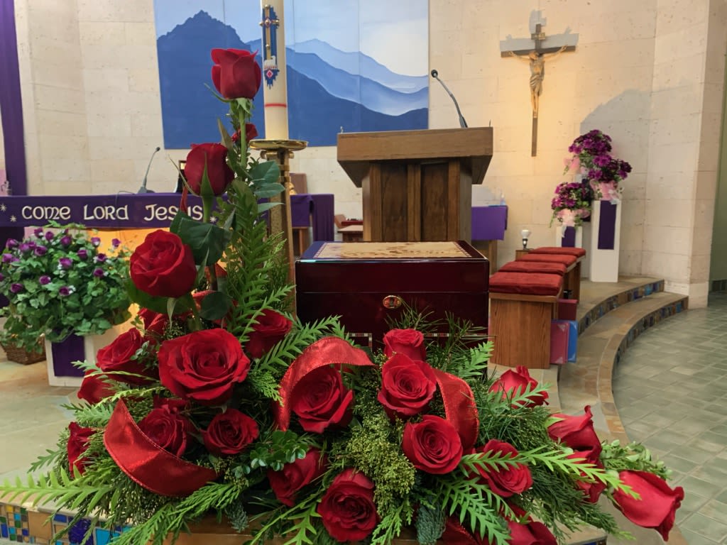 Red roses arranged in a church setting with red ribbon accents