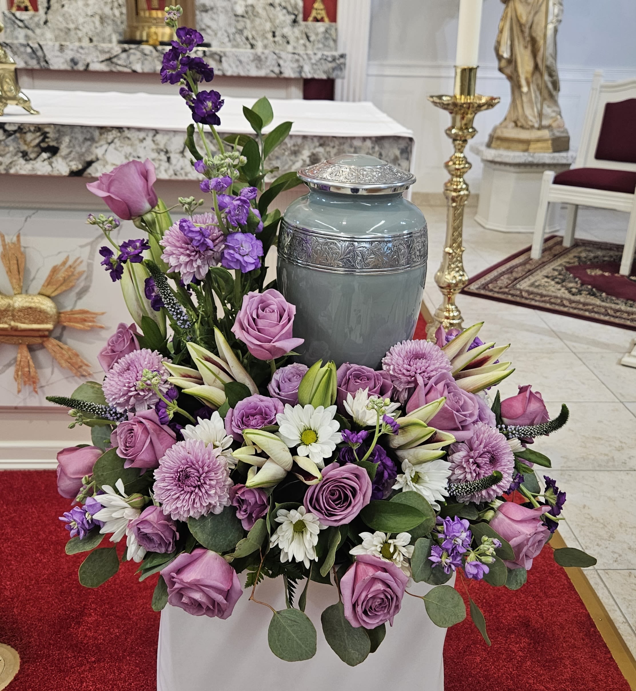 Lavender and white floral arrangement around a gray urn in a church
