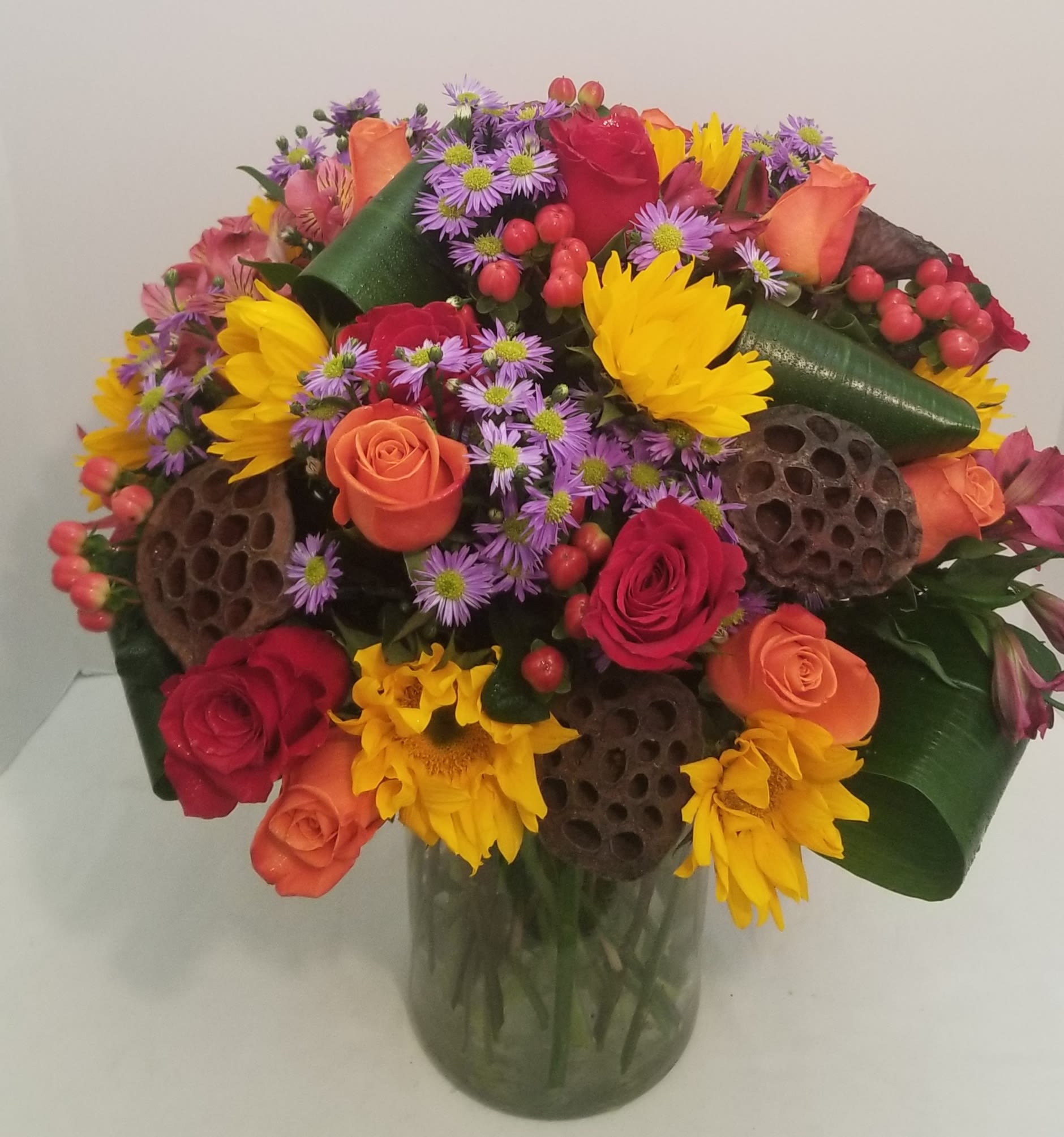 Mixed bouquet of roses, sunflowers, and purple daisies in a glass vase