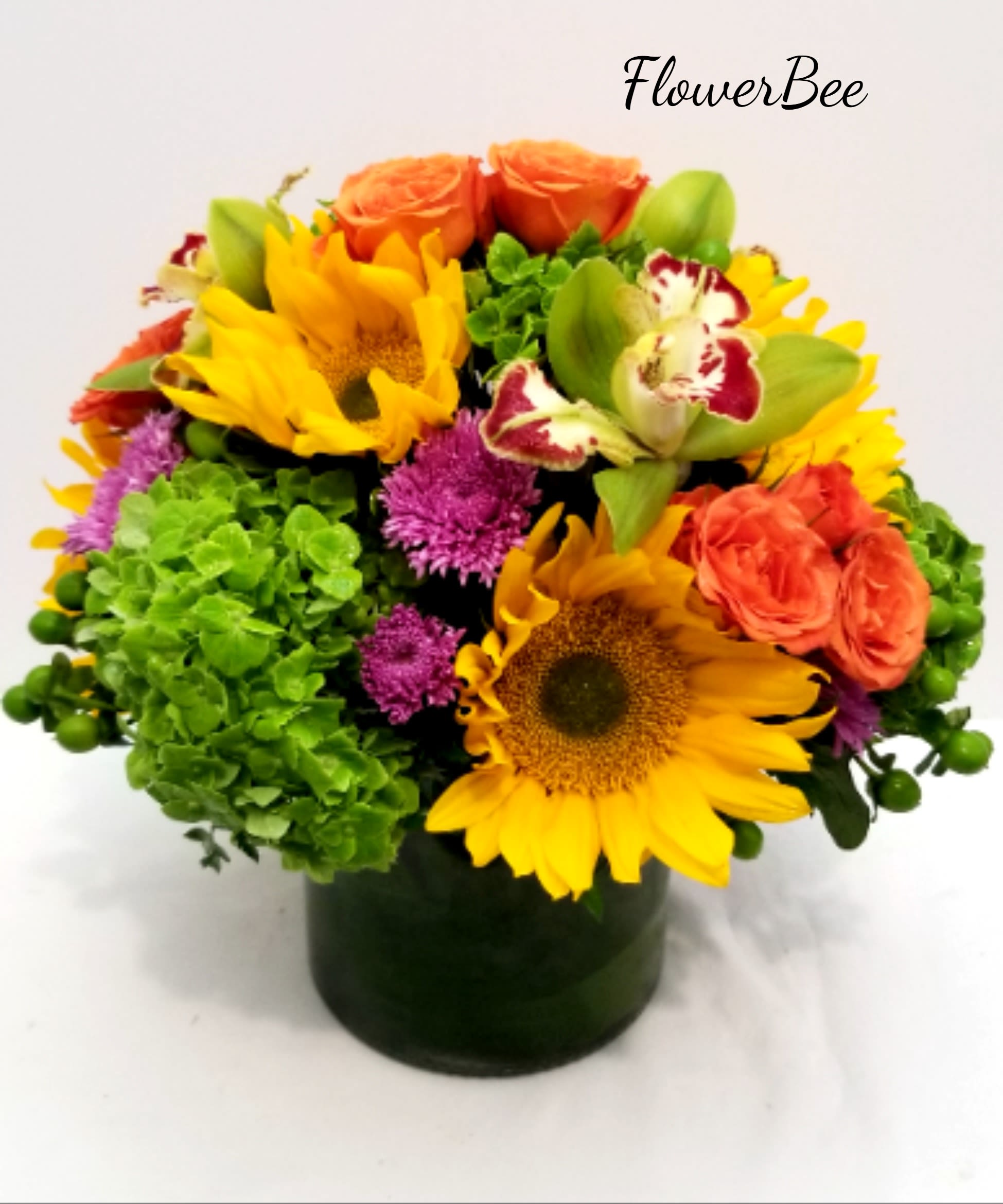 Colorful arrangement of sunflowers, orange roses, green hydrangeas, and orchids in a cylinder vase
