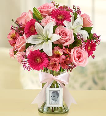 Sweet Baby Girl Arrangement - A precious gift to congratulate the proud new parents of a sweet baby girl! Hand-crafted by our team of skilled designers using only the freshest roses, mini Gerberas, lilies, mini carnations and more, then beautifully gathered in a classic clear vase featuring a mini magnetic photo frame and pink bow This is one surprise sure to leave them smiling! Lilies may arrive in bud form and will open to full beauty over the next 2-3 day. Our florists hand-design each arrangement, so colors, varieties and container may vary due to local availability.  To request a specific color scheme, please note in special instructions.