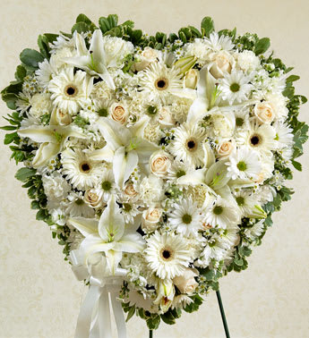 White Heart - This solid heart standing spray makes a beautiful statement about your heartfelt compassion and sympathy. White flowers such as roses, lilies, Gerbera daisies, carnations and more.  Solid heart with oasis, tied to the wire easel with satin ribbon Sent directly to the funeral home by family, friends and business associates Our florists use only the freshest flowers available so components may vary. To request a specific color scheme, please note in special instructions