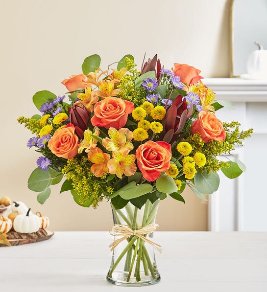 Autumn Breeze - Our bouquet captures this sentiment in a beautiful way. Rich red, orange and yellow blooms are loosely gathered with lush greenery for an abundance of style and texture.All-around arrangement with orange roses and Peruvian lilies (alstroemeria), red Leucadendron, yellow button poms and purple monte casino; accented with silver dollar eucalyptus and assorted greenery