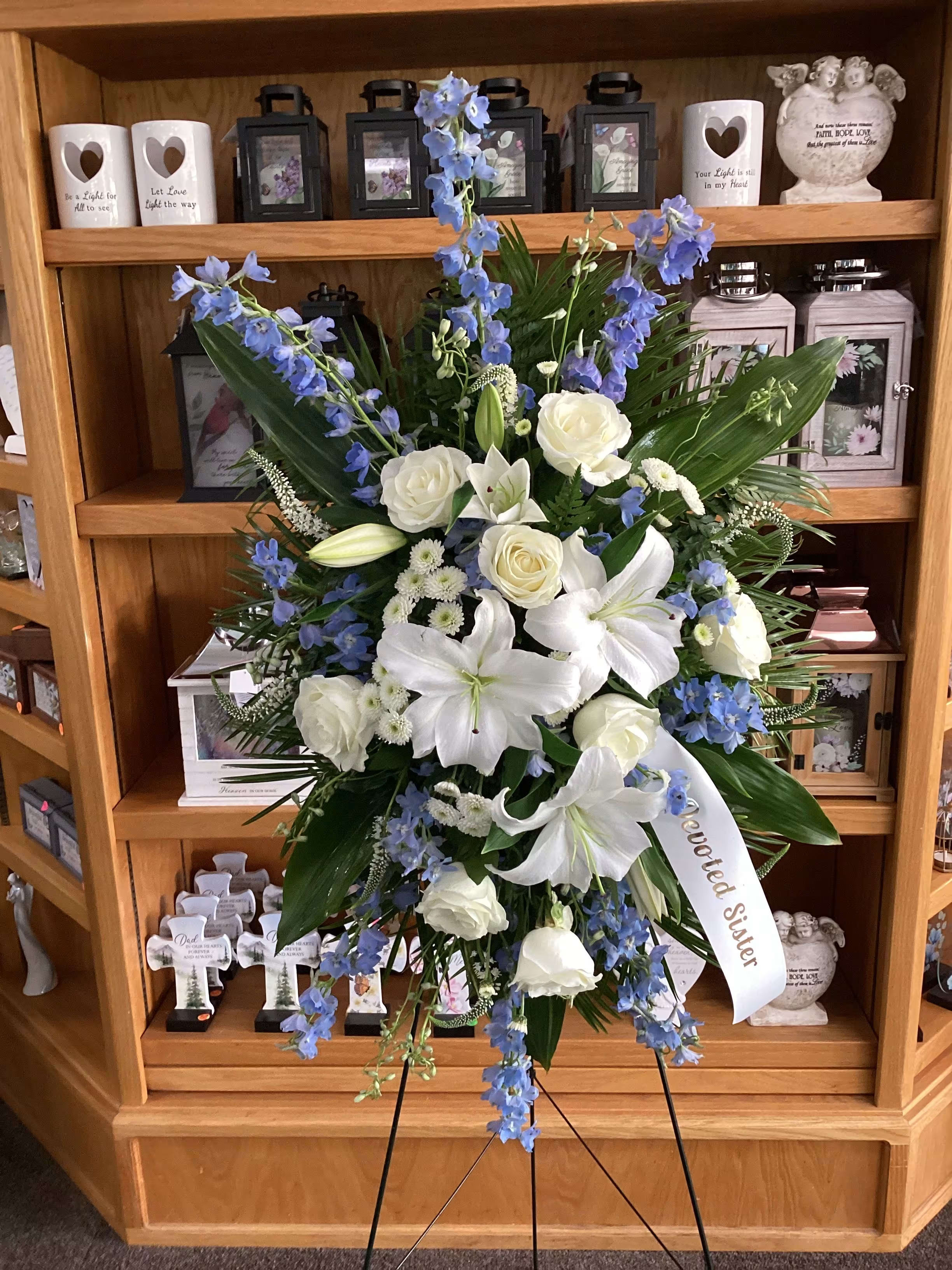 Standing sympathy spray with white lilies, roses, and blue flowers on an easel