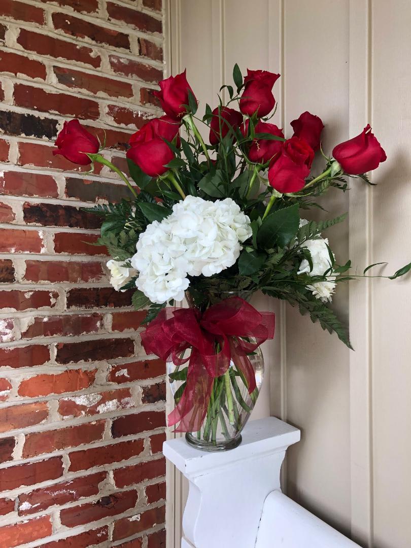 Red roses and white hydrangeas in a clear glass vase with a red ribbon
